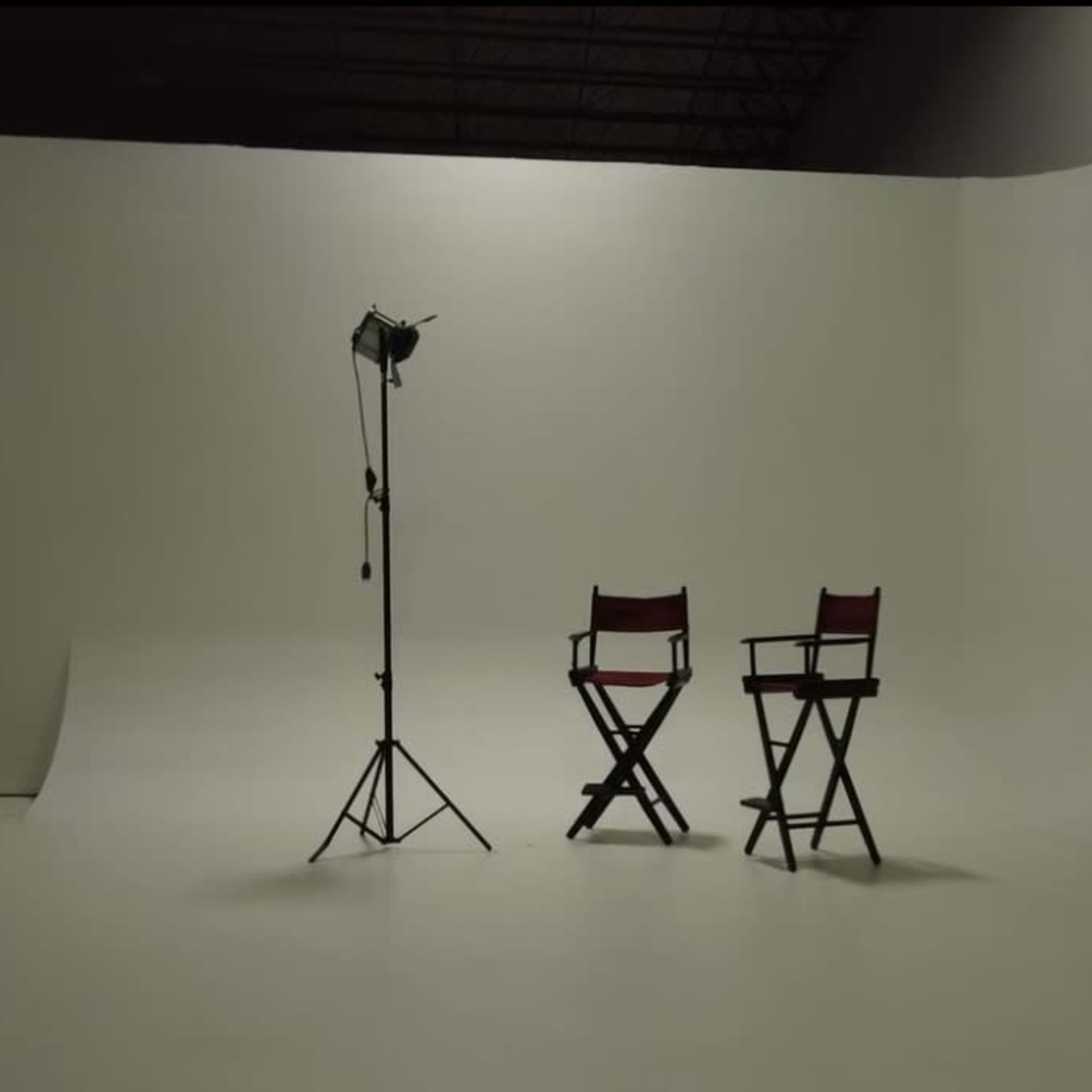A photography studio features two red director's chairs beside a standing light on a plain white backdrop.
