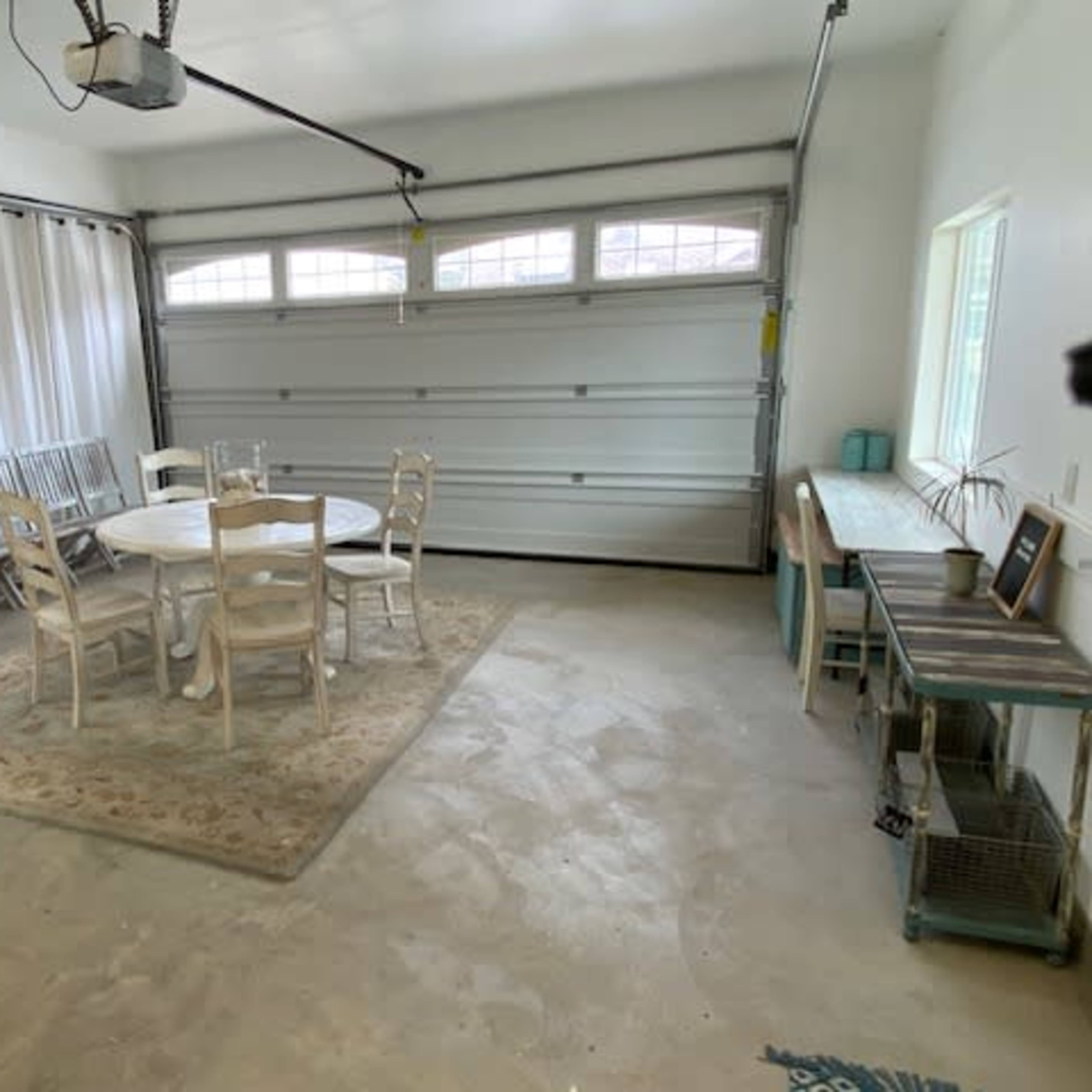 A garage featuring a circular dining table with six chairs, a refrigerator, and a console table against the wall.