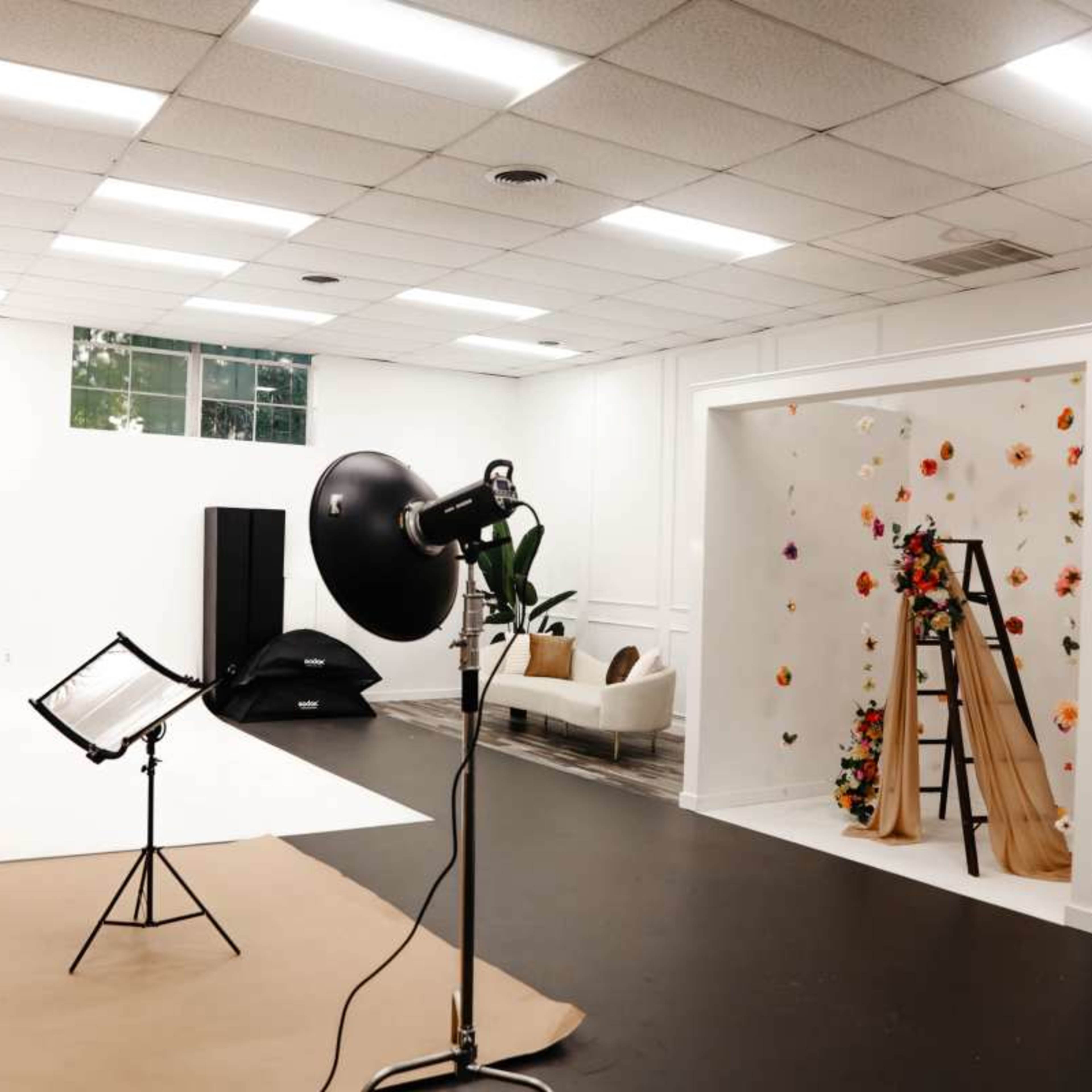 A photography studio with a backdrop, lighting equipment, and an area decorated with flowers and a ladder.