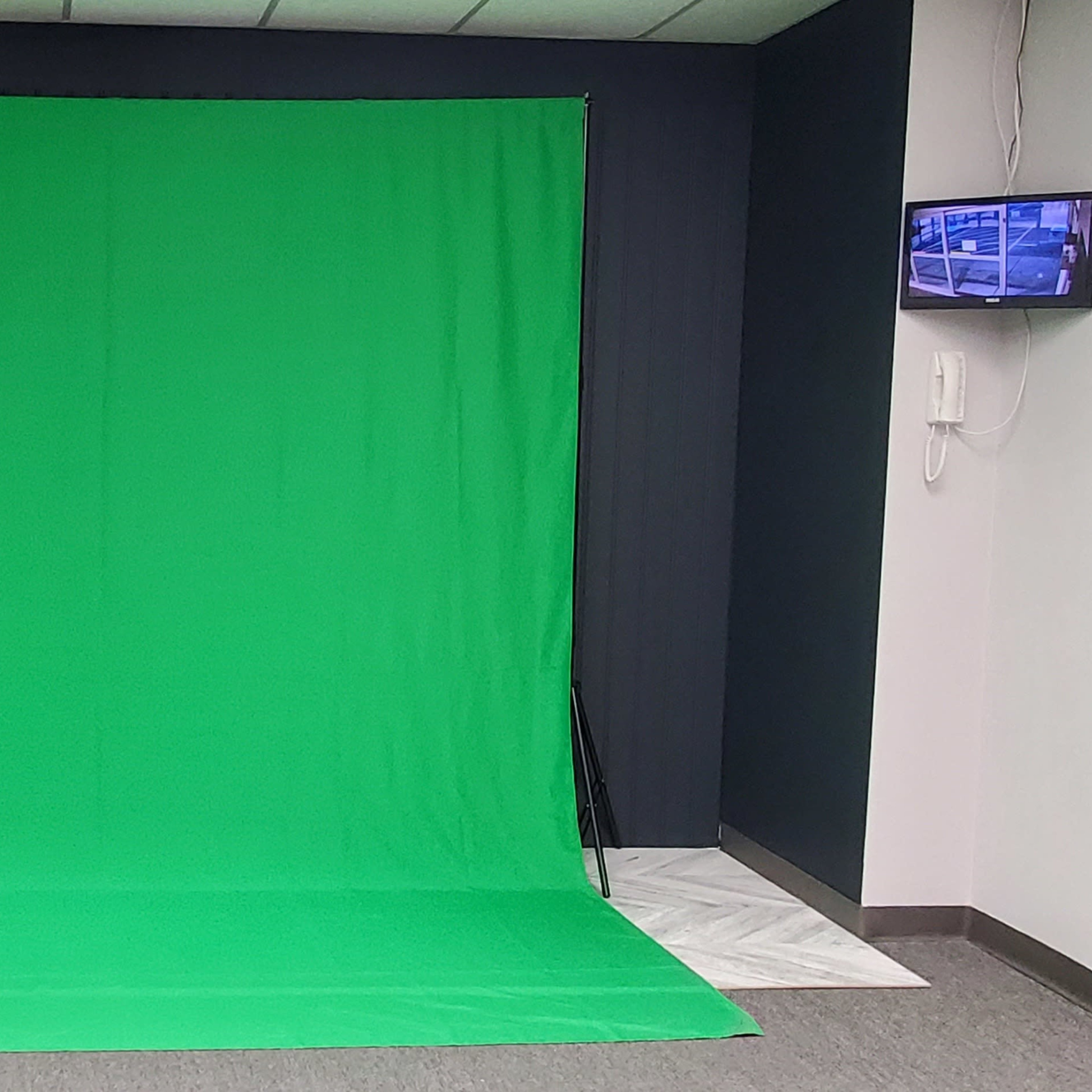 A green backdrop set up in a room, with a flat surface and a small screen mounted on the wall.