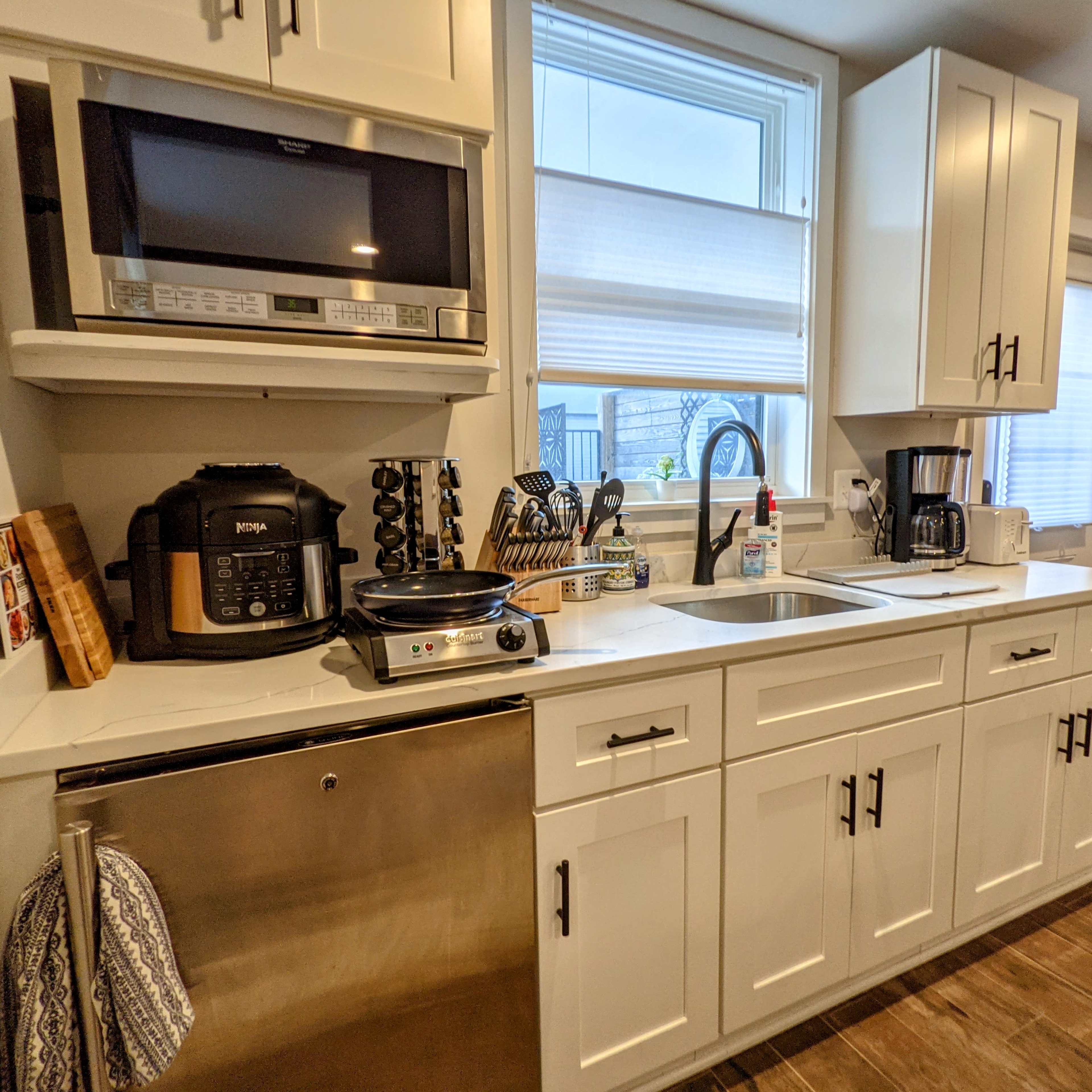 A modern kitchen features white cabinets, a stainless steel refrigerator, and various appliances including a microwave and coffee maker.