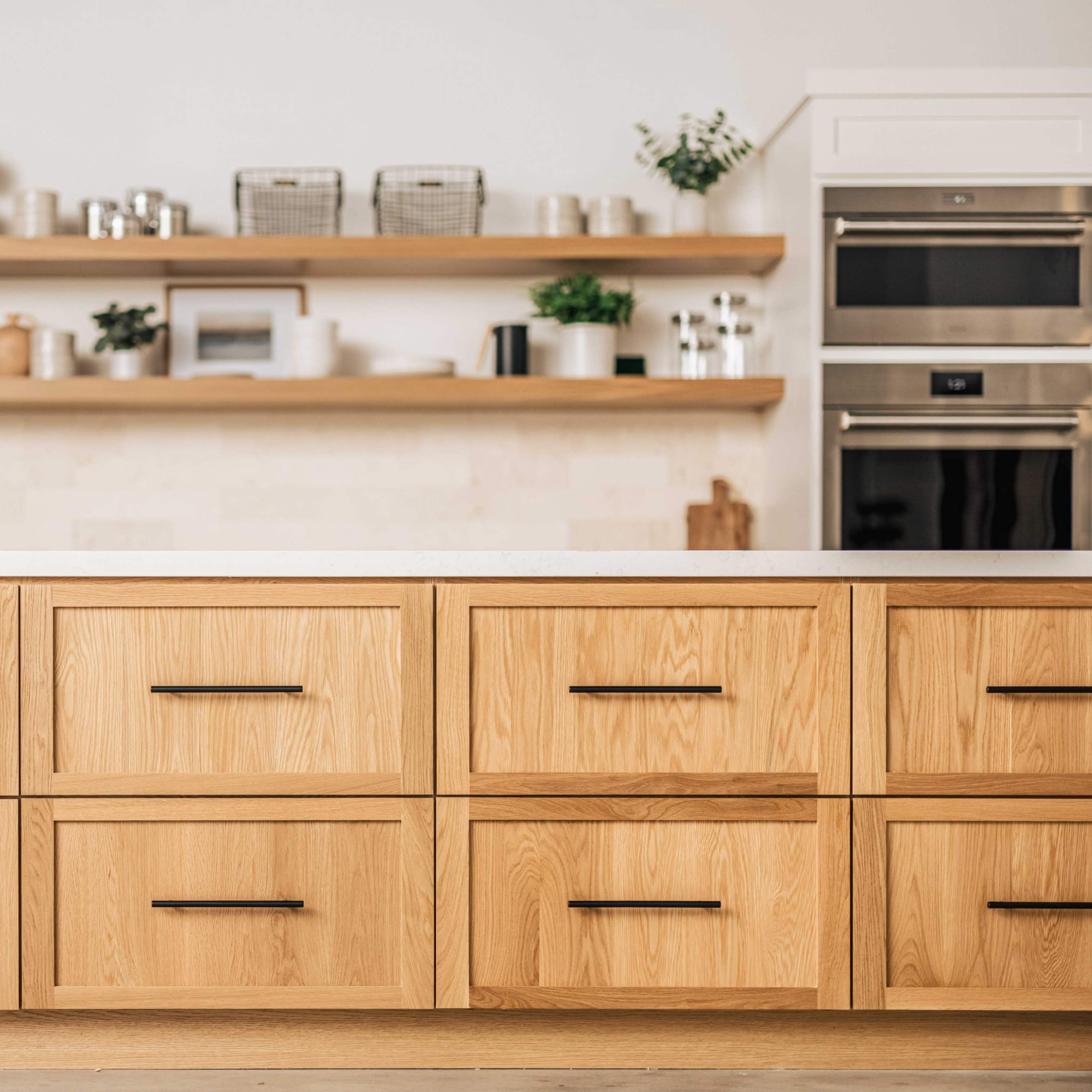 A modern kitchen with a wooden drawer cabinet, a countertop, and open shelving above displaying various kitchen items.
