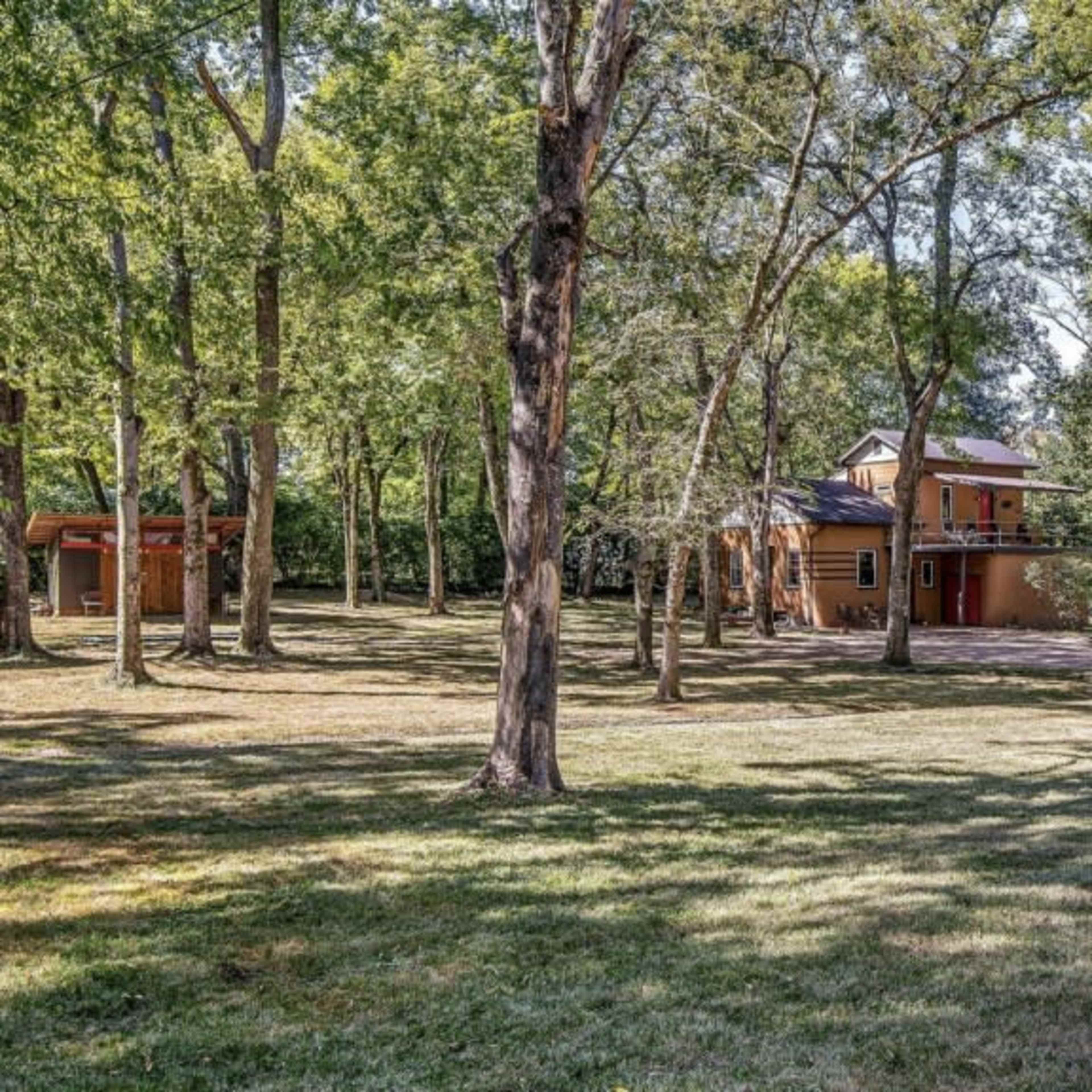 A two-story house is set among tall trees in a grassy area.