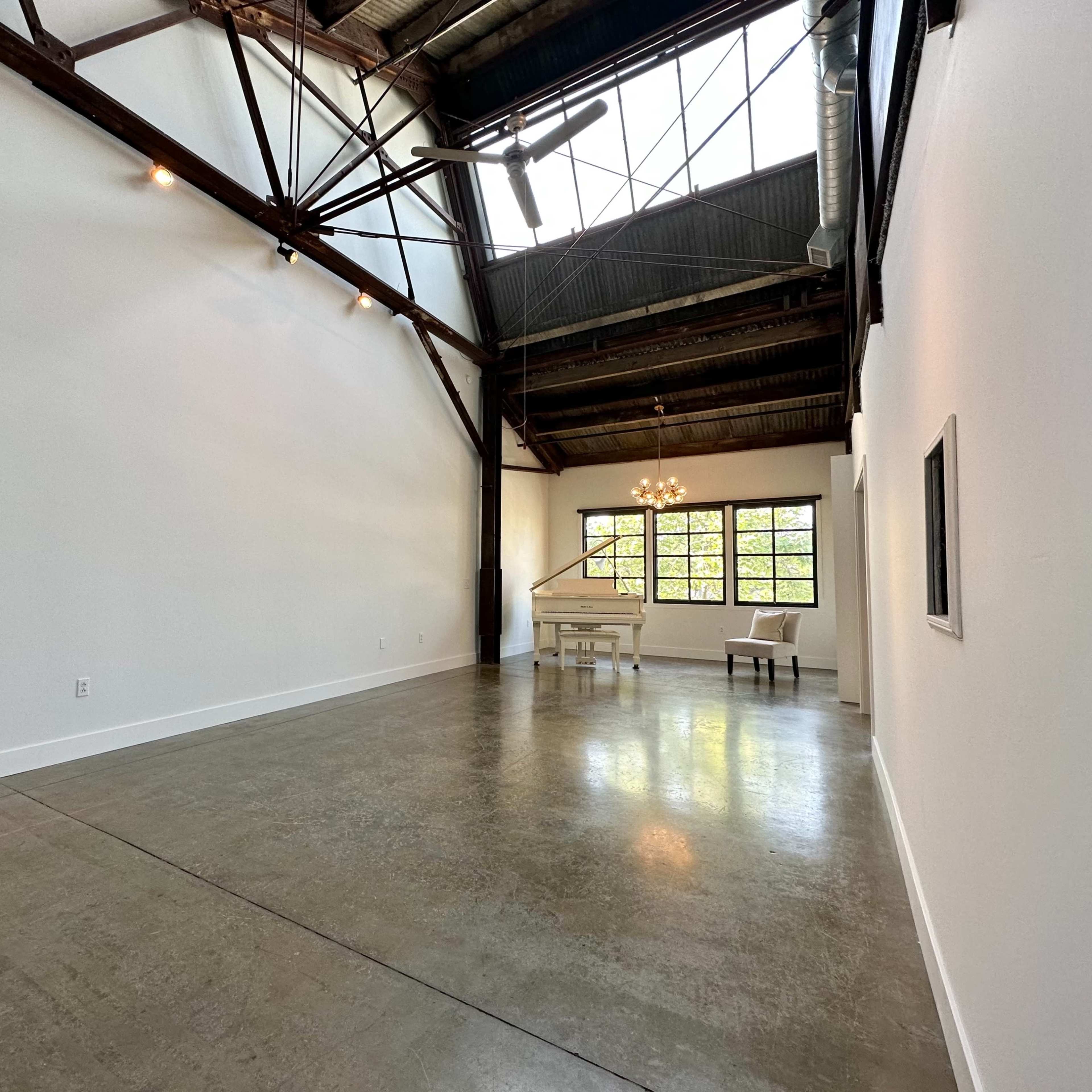 A spacious, industrial-style room with tall windows, exposed beams, and a minimalist dining area.