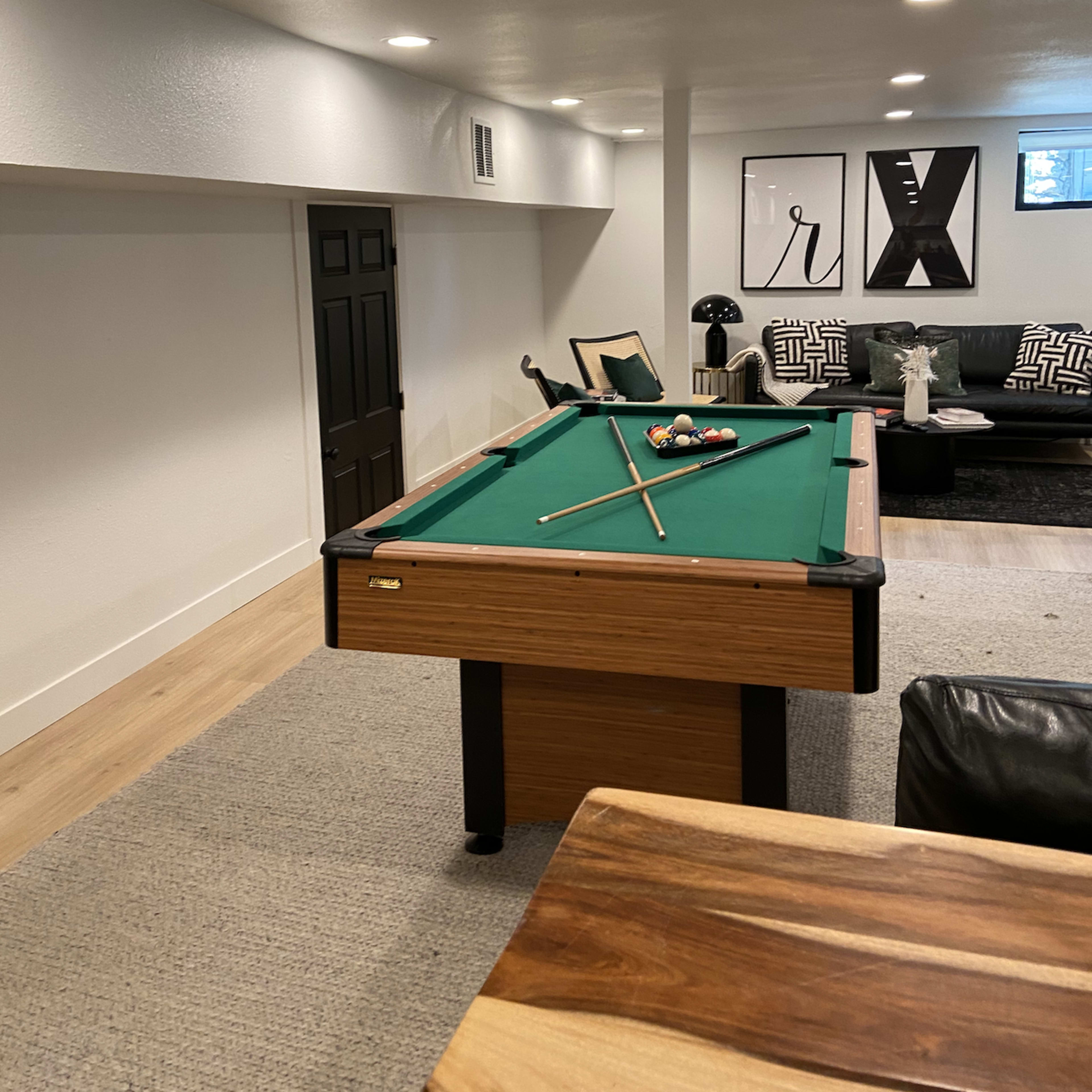 A basement game room featuring a pool table, a black door, and a seating area with a couch and decorative wall art.