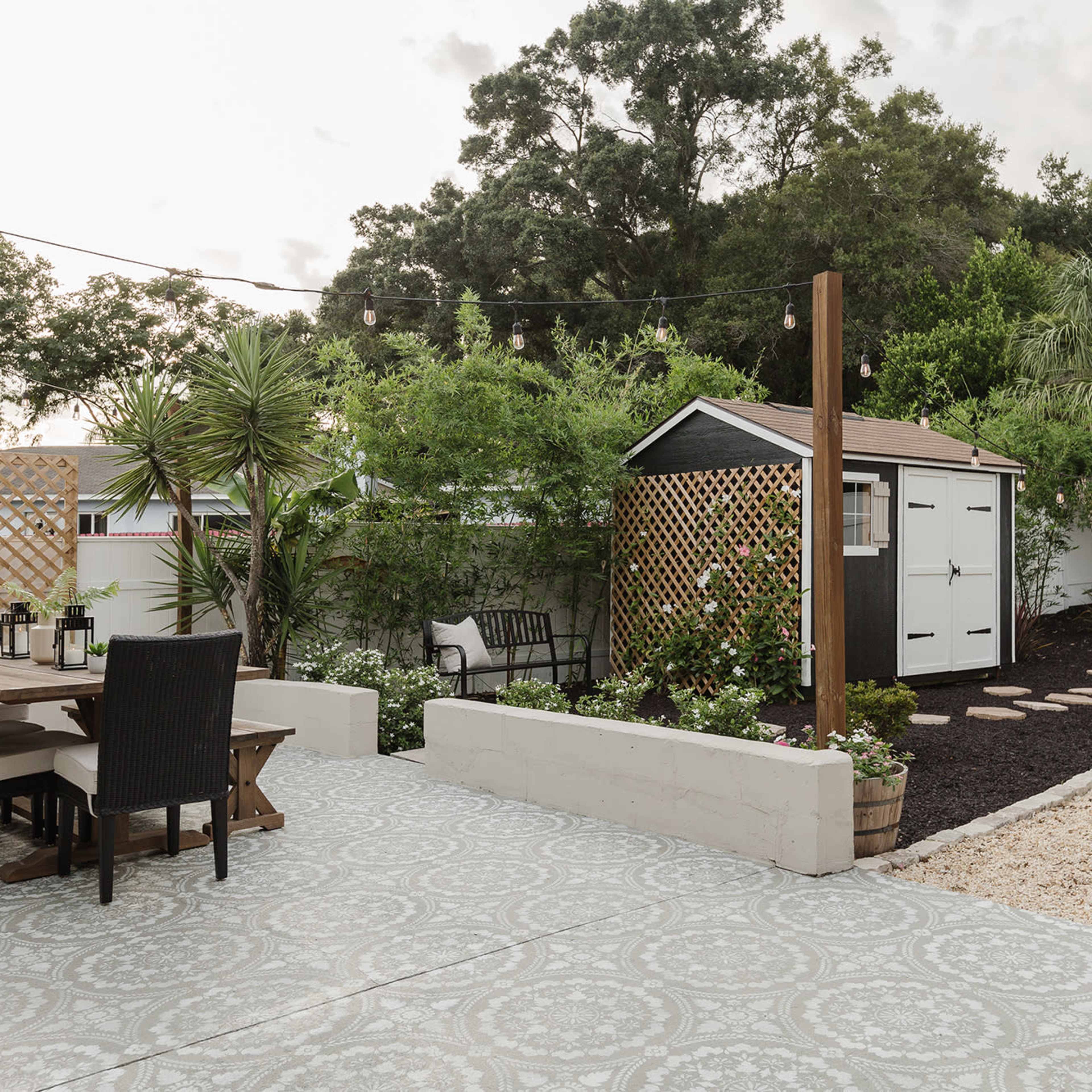 A well-designed backyard with a dining set, a shed, lush greenery, and a pathway lined with gravel and plants.
