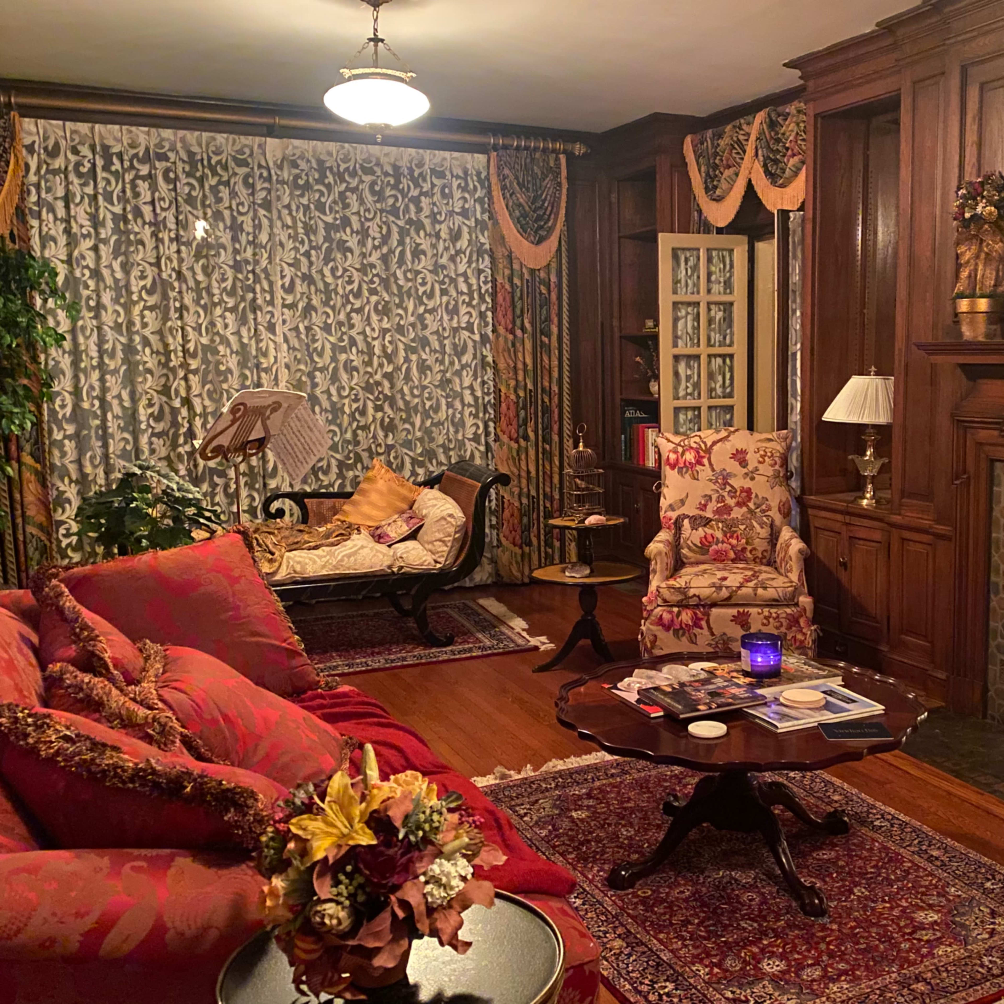 A cozy living room with floral upholstered furniture, a wooden fireplace, and decorative curtains.