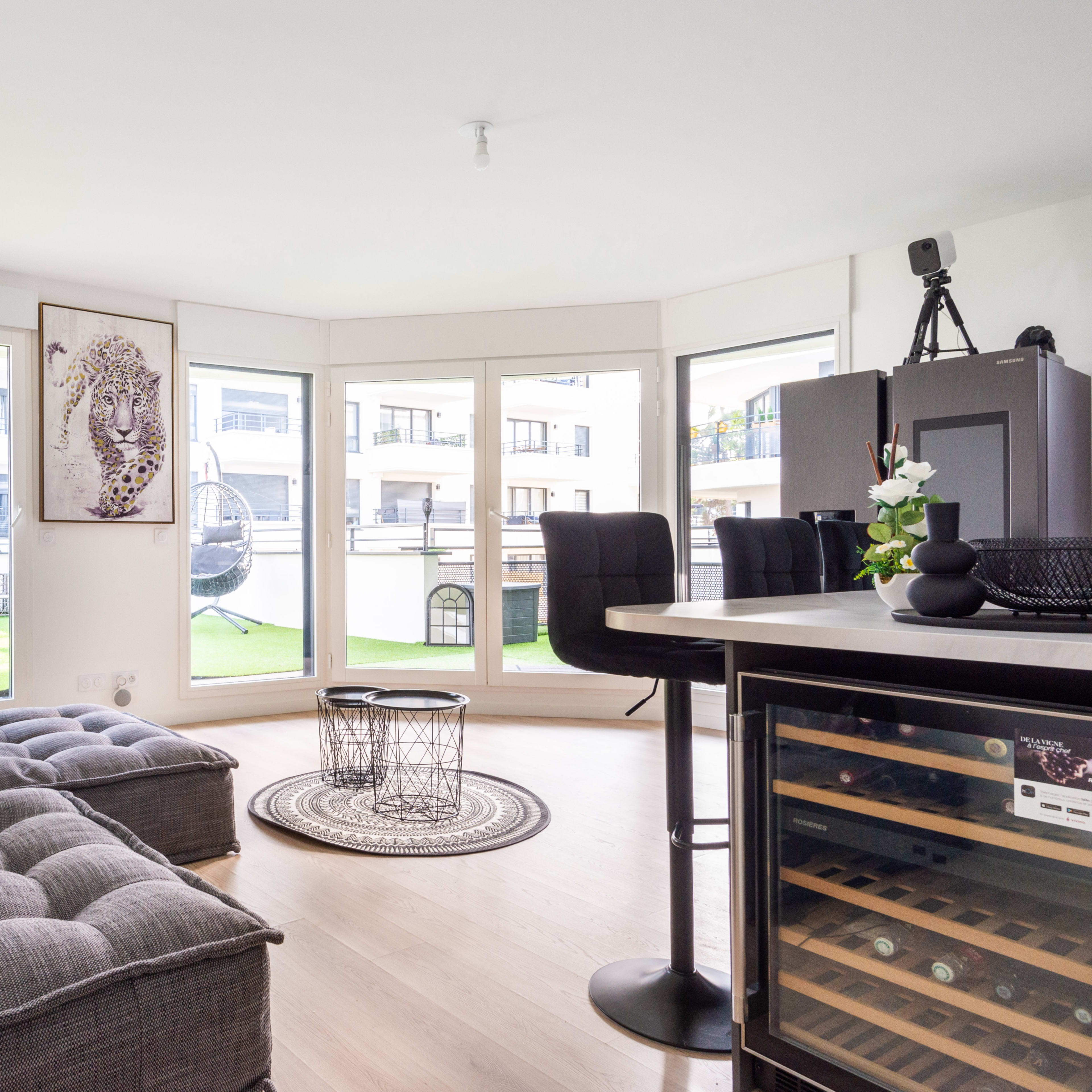 A modern living space with a gray upholstered sofa, a round rug, and a view of a green outdoor area through large windows.