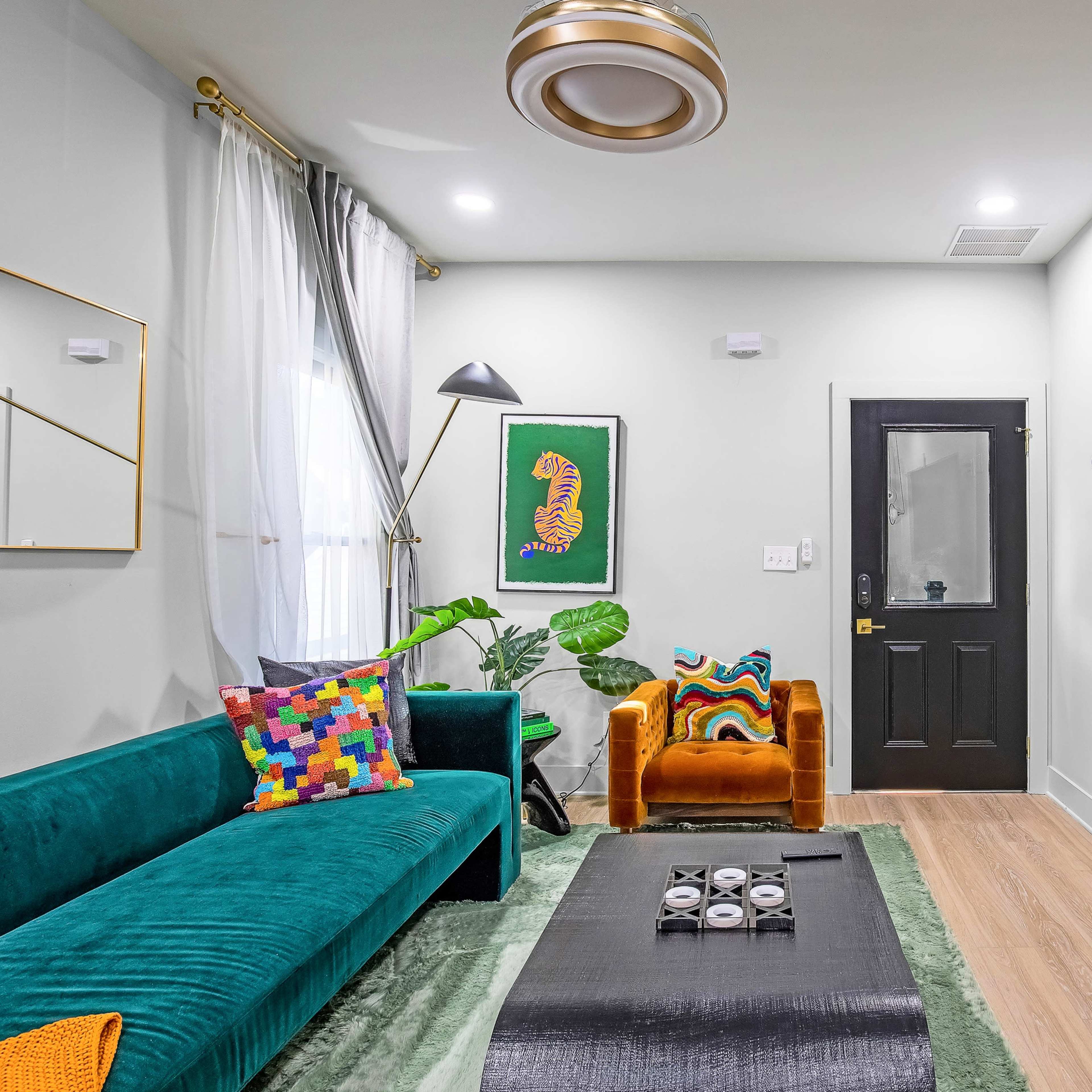 The living room features a teal sofa, an orange chair, a coffee table, and vibrant decor against light walls and wooden flooring.