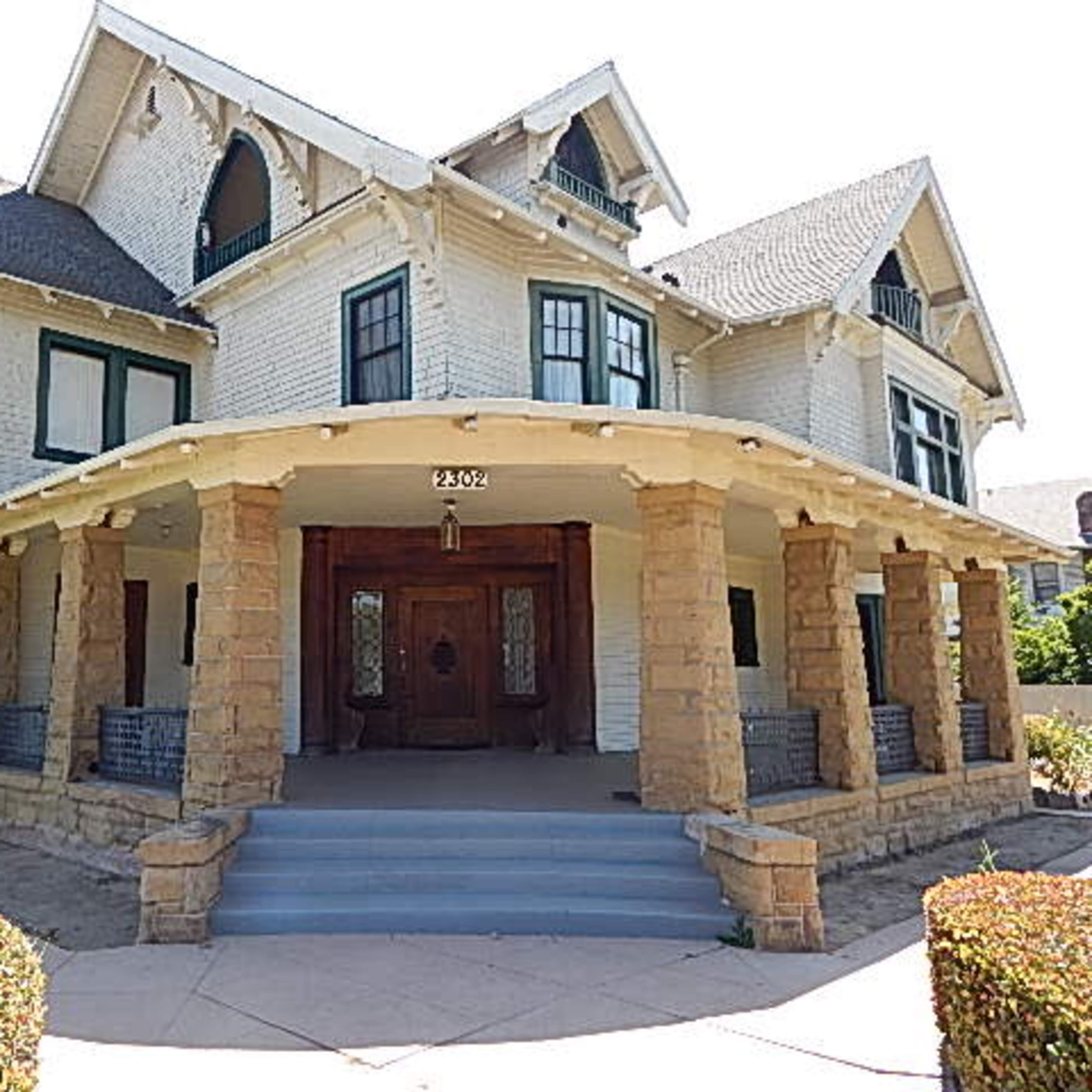 A large, two-story Victorian-style house with a prominent porch, stone pillars, and multiple gabled roofs.