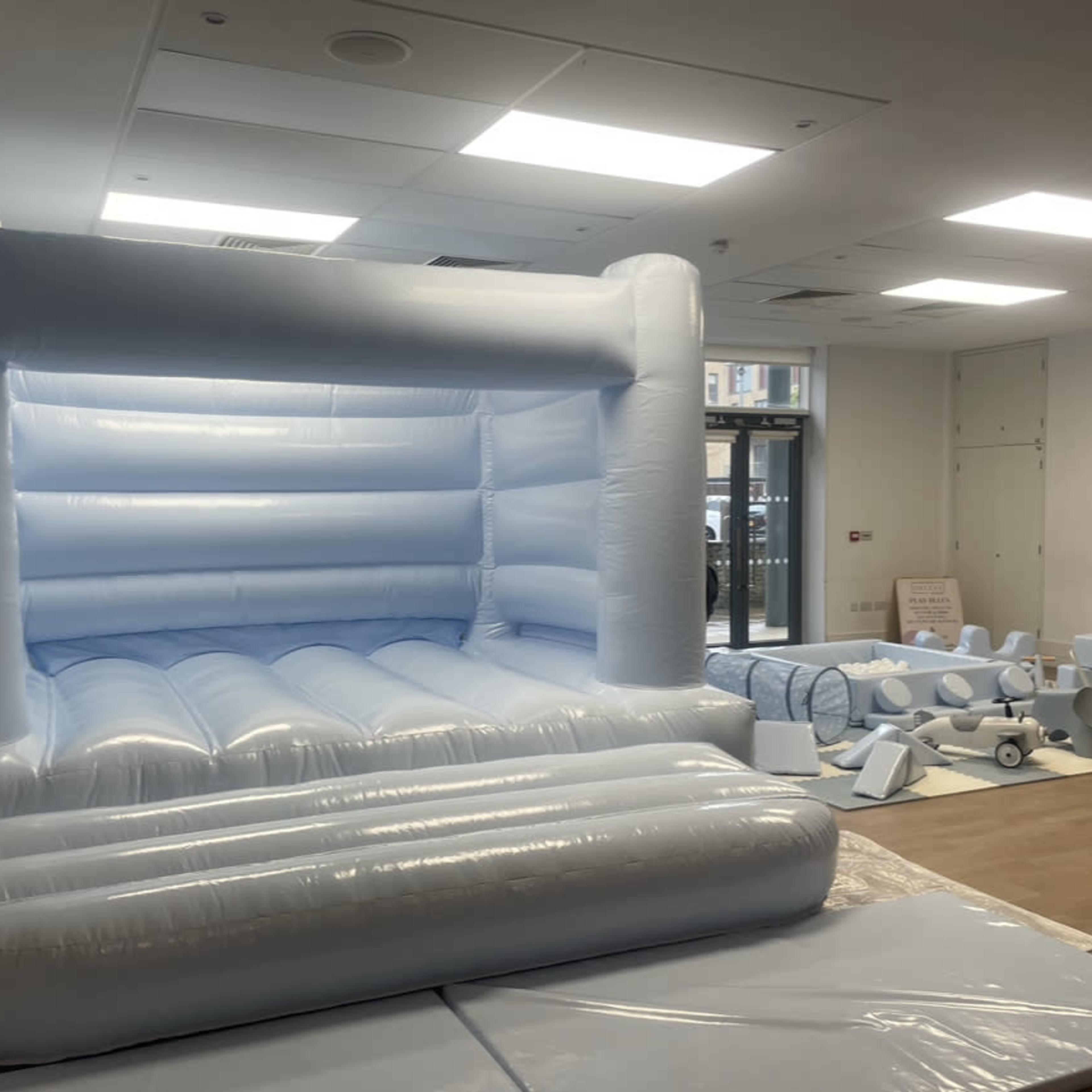 A large blue inflatable bouncy castle set up in a room, with various pieces of foam padding arranged nearby.