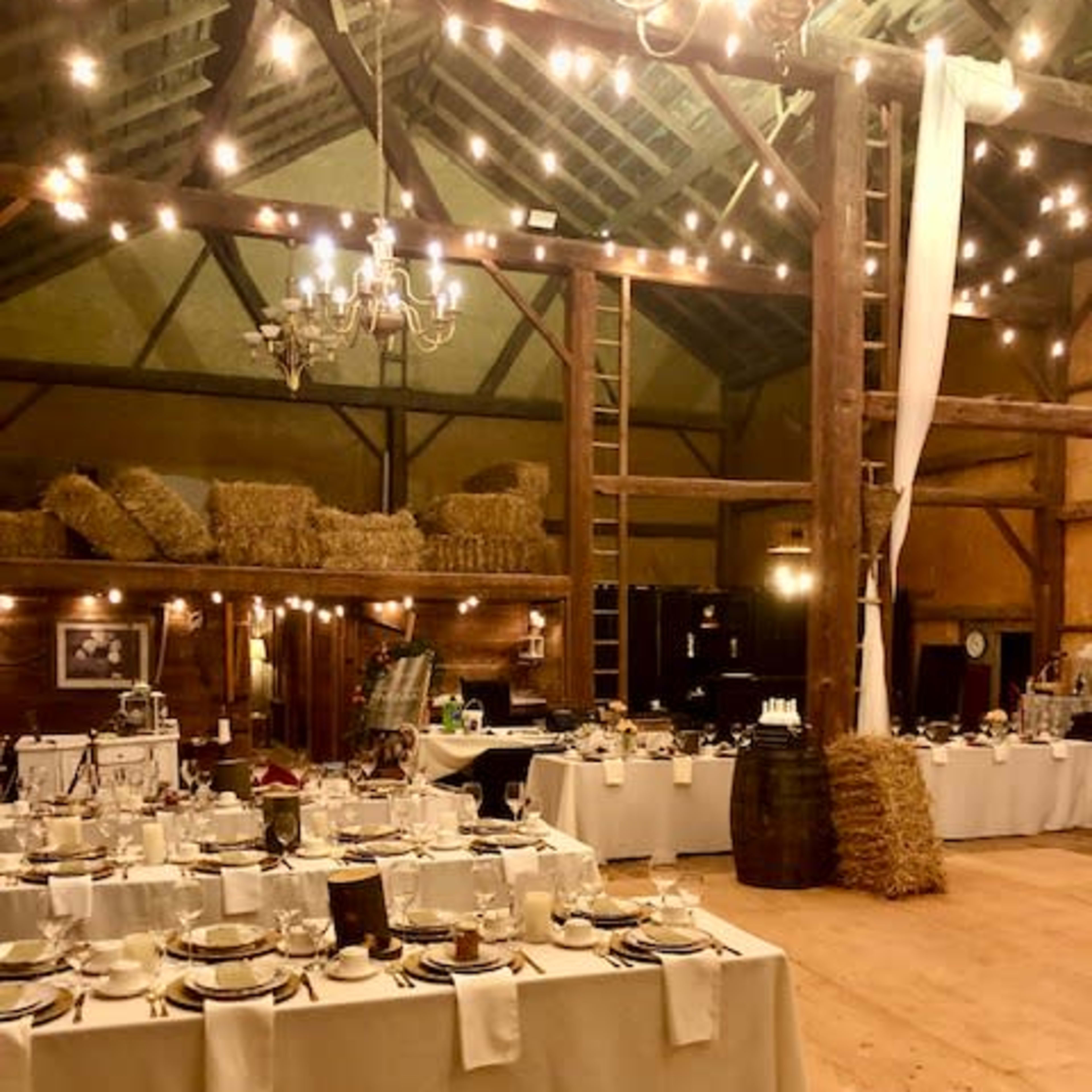 A rustic banquet hall with elegantly set tables, string lights, and wooden beams.