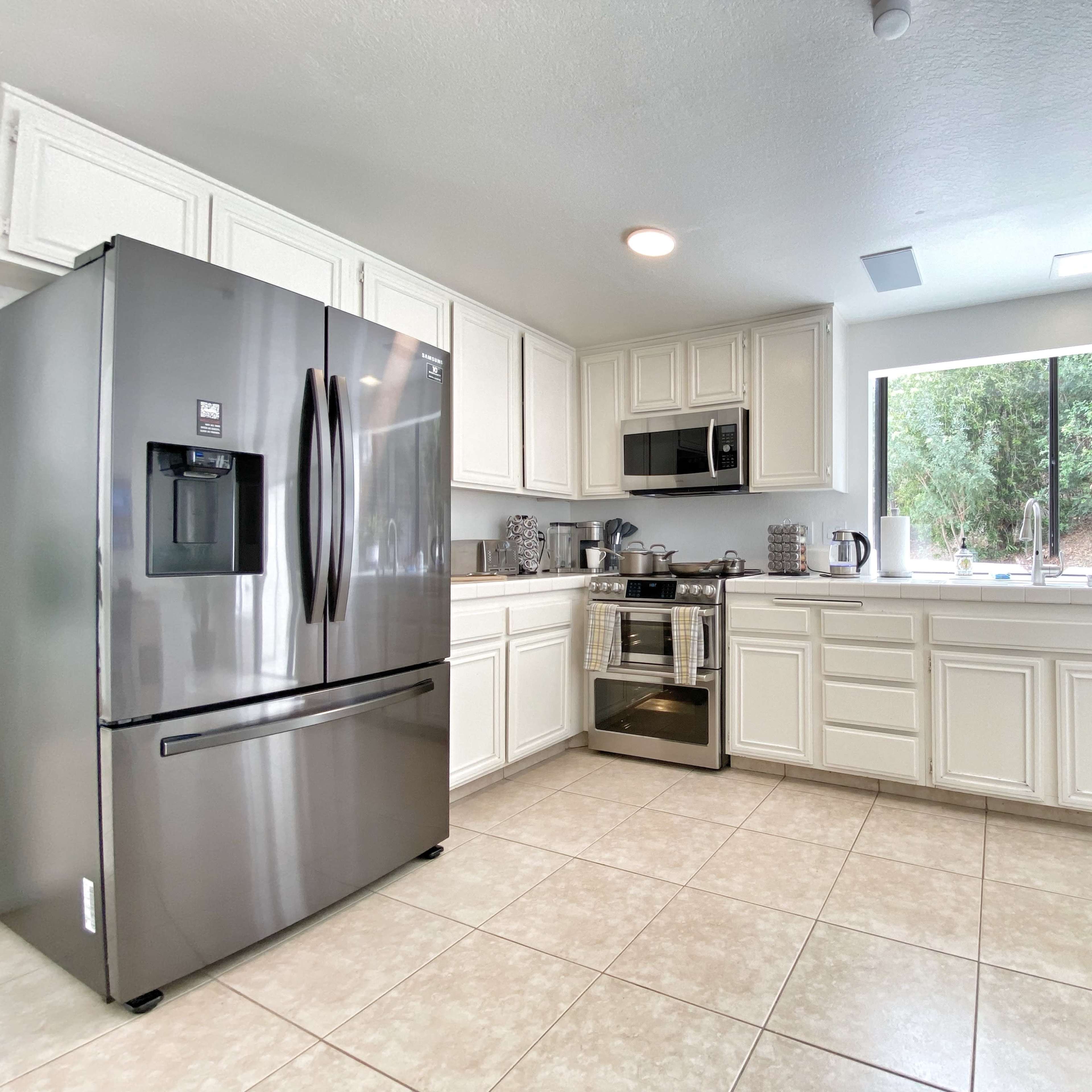 The kitchen features white cabinets, stainless steel appliances, a large window with outdoor views, and tiled flooring.