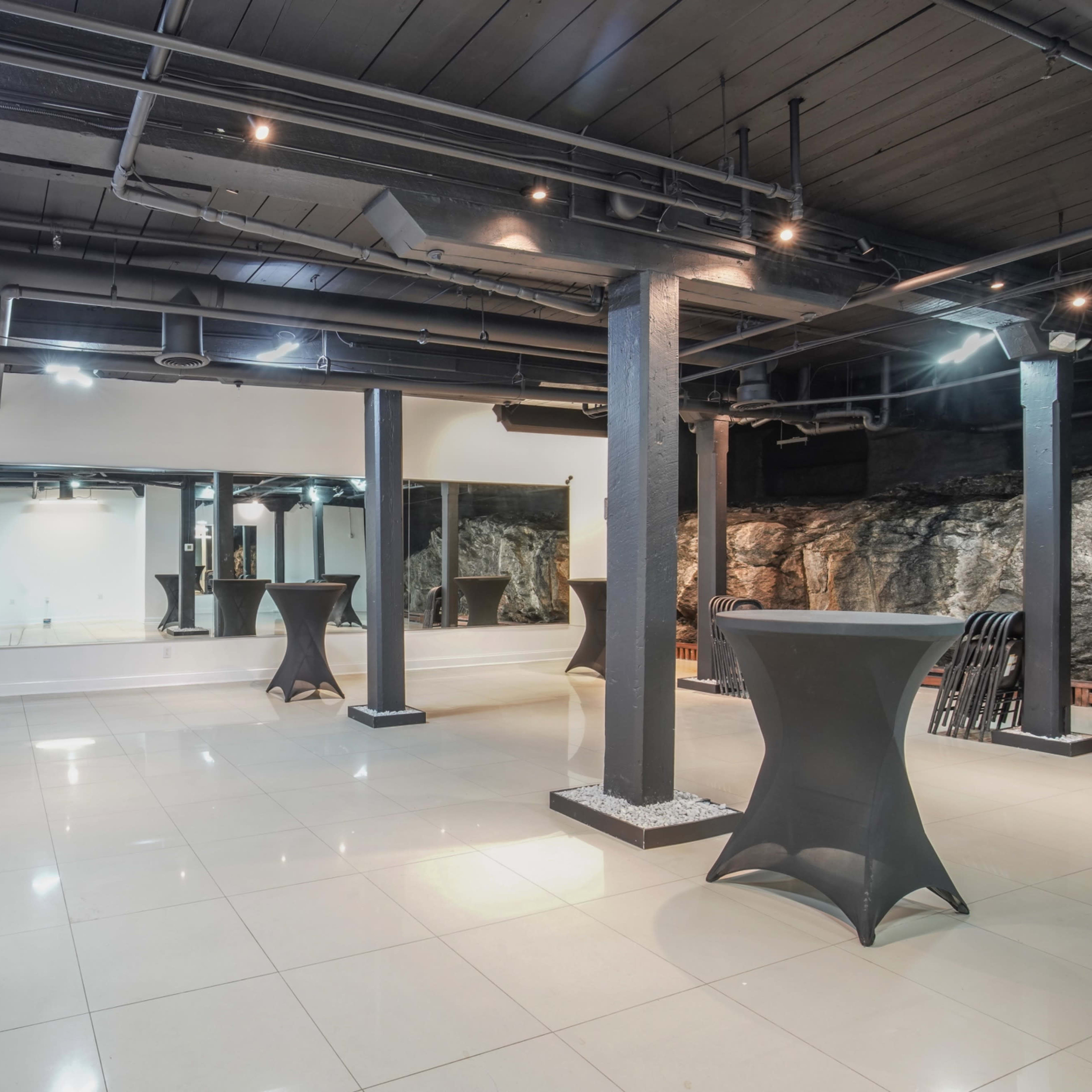 A spacious indoor area with black columns, tiled flooring, and multiple lighting fixtures, alongside mirrored walls and decorative features.