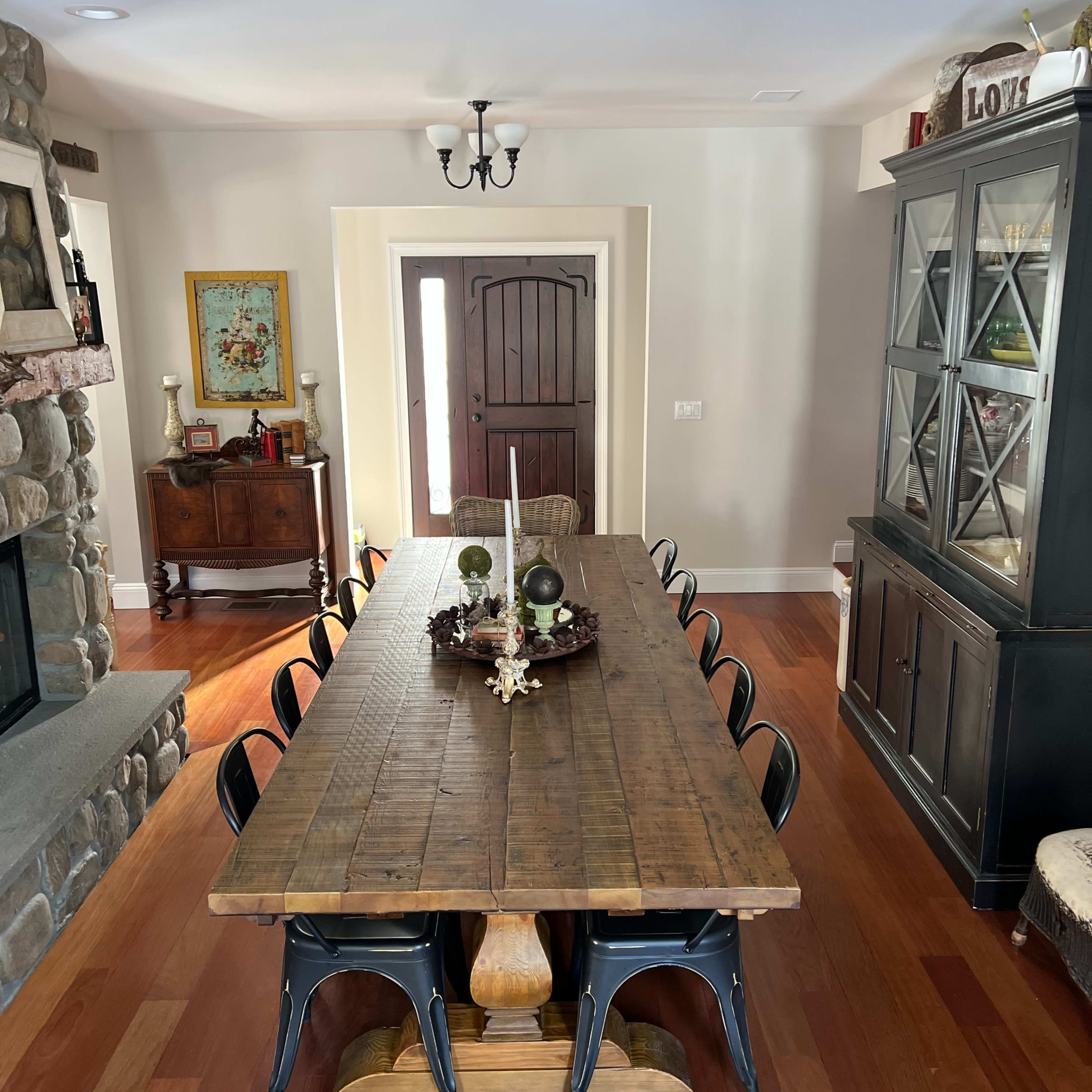 A long wooden dining table with black chairs is set in a room featuring a stone fireplace, a large cabinet, and a decorative wooden door.