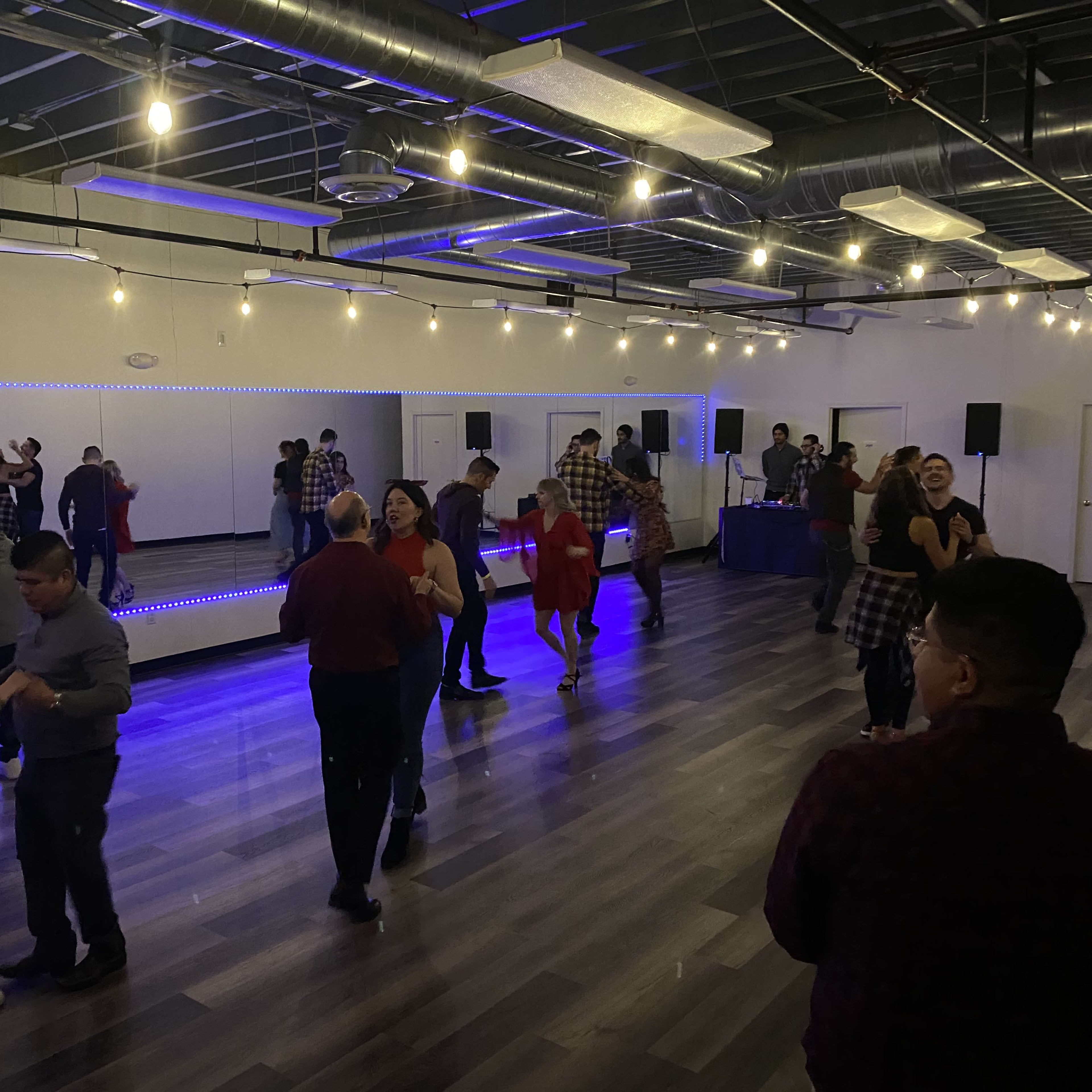 A lively dance event takes place in a spacious room with mirrored walls and colorful lights.
