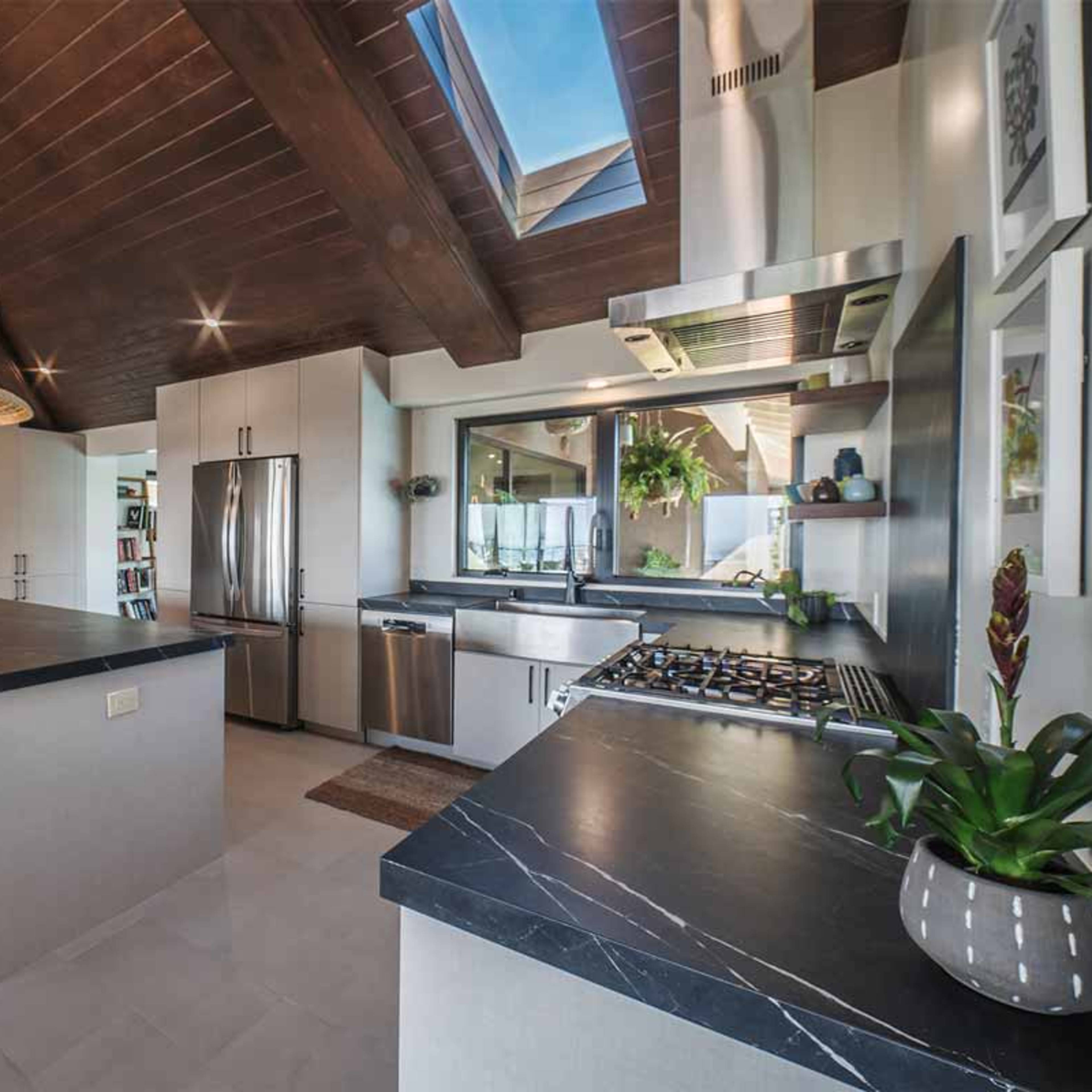 A modern kitchen with open shelving, a large dark countertop island, woven pendant lights, and stainless steel appliances.