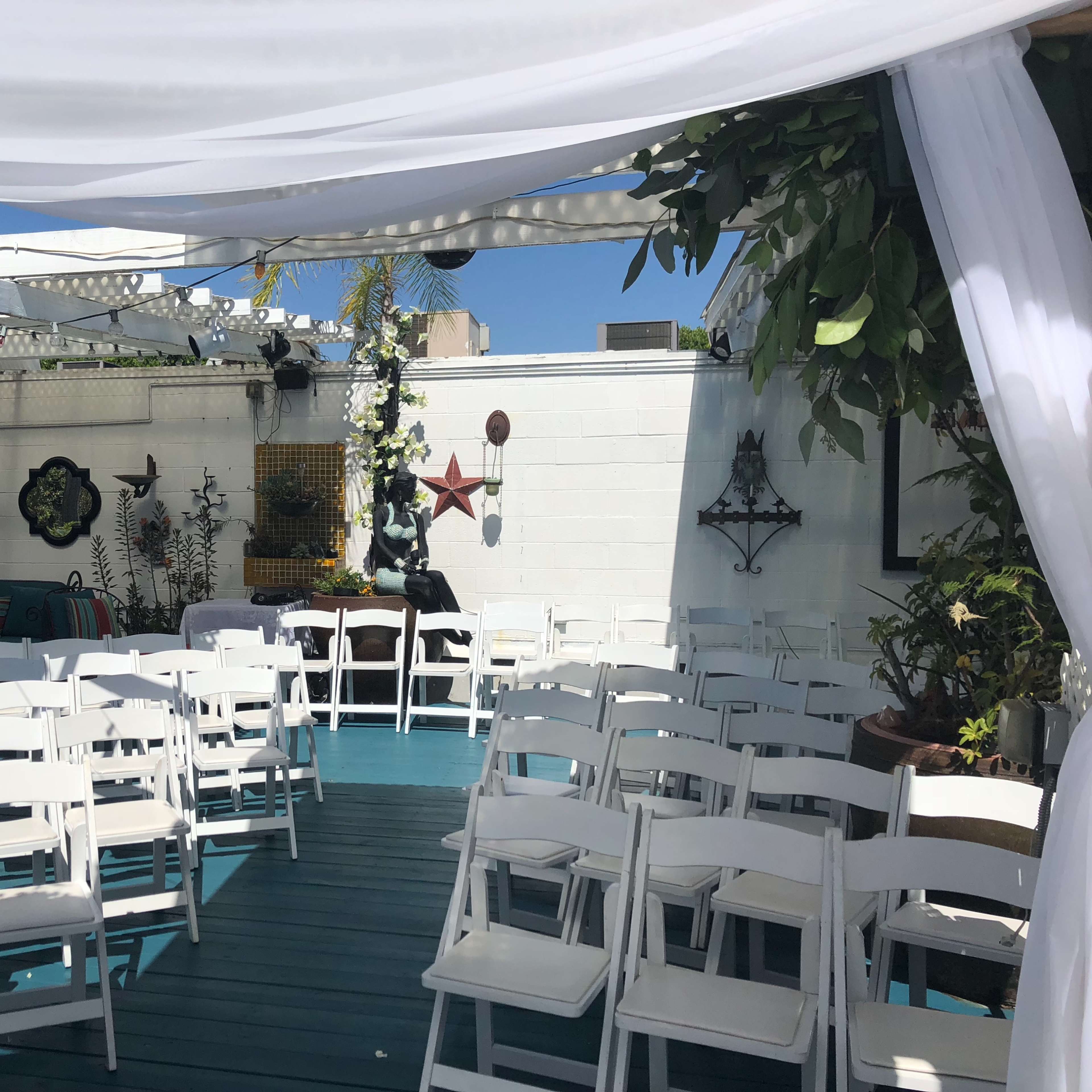 A decorated outdoor space with white chairs set up for an event beneath a canopy.