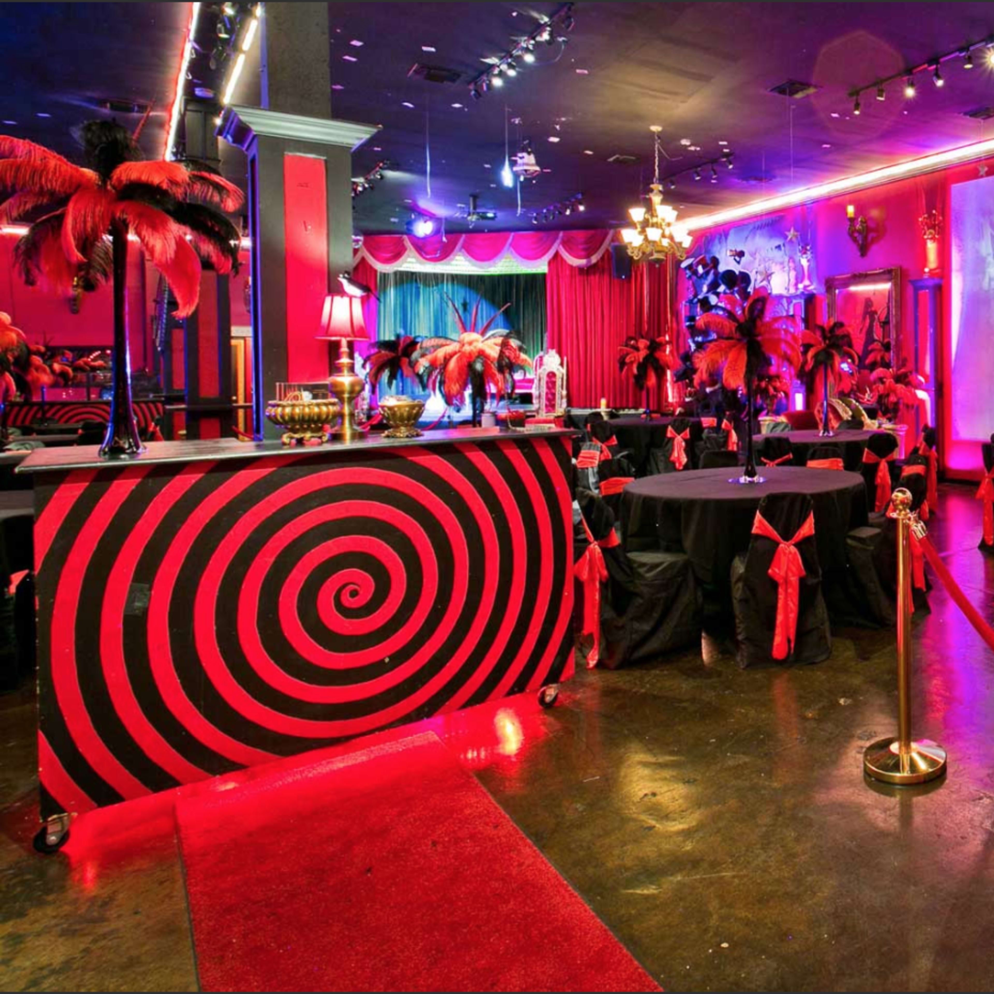 A vibrant party venue featuring a black and red color scheme, with a spiral-patterned bar, elegant seating, and decorative palm trees.