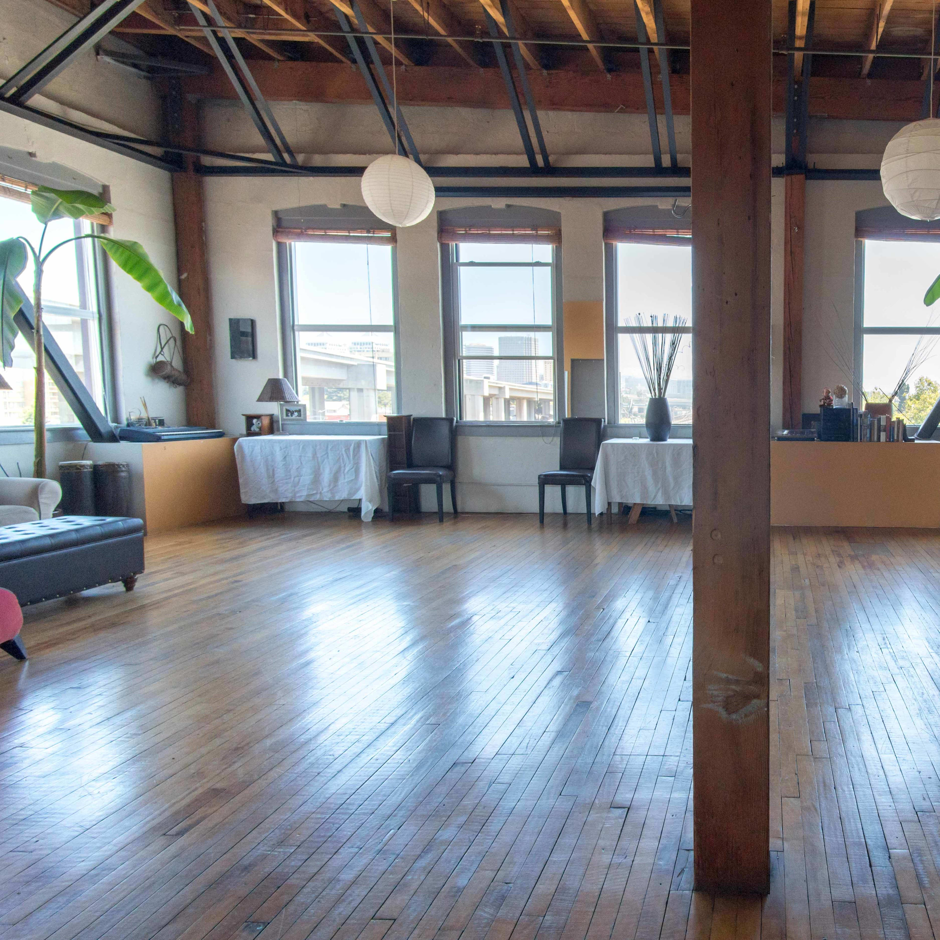 The room features hardwood floors, large windows with natural light, and a central wooden support column, with tables and chairs arranged on either side.