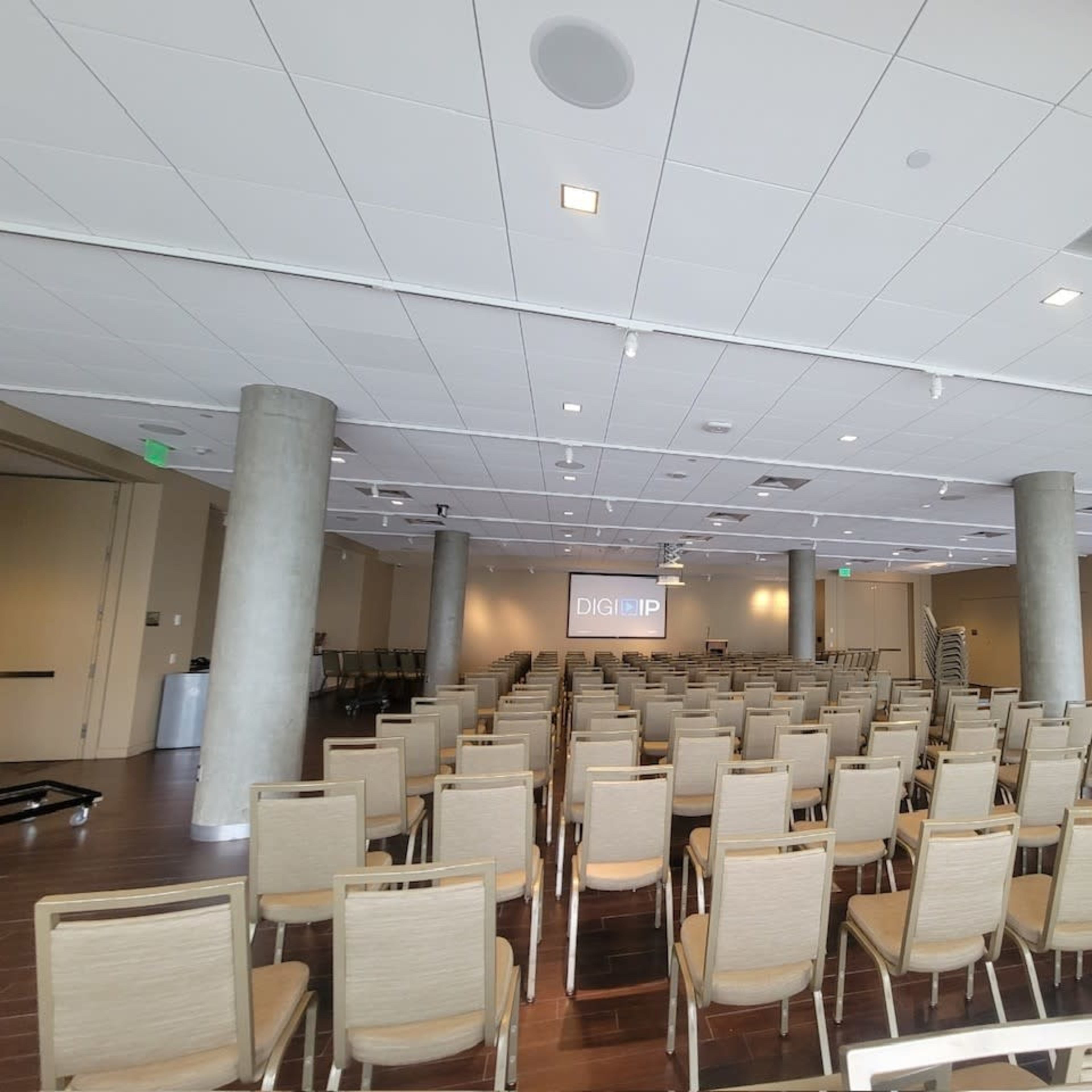 A conference room set up with rows of empty chairs facing a projector screen at the front.