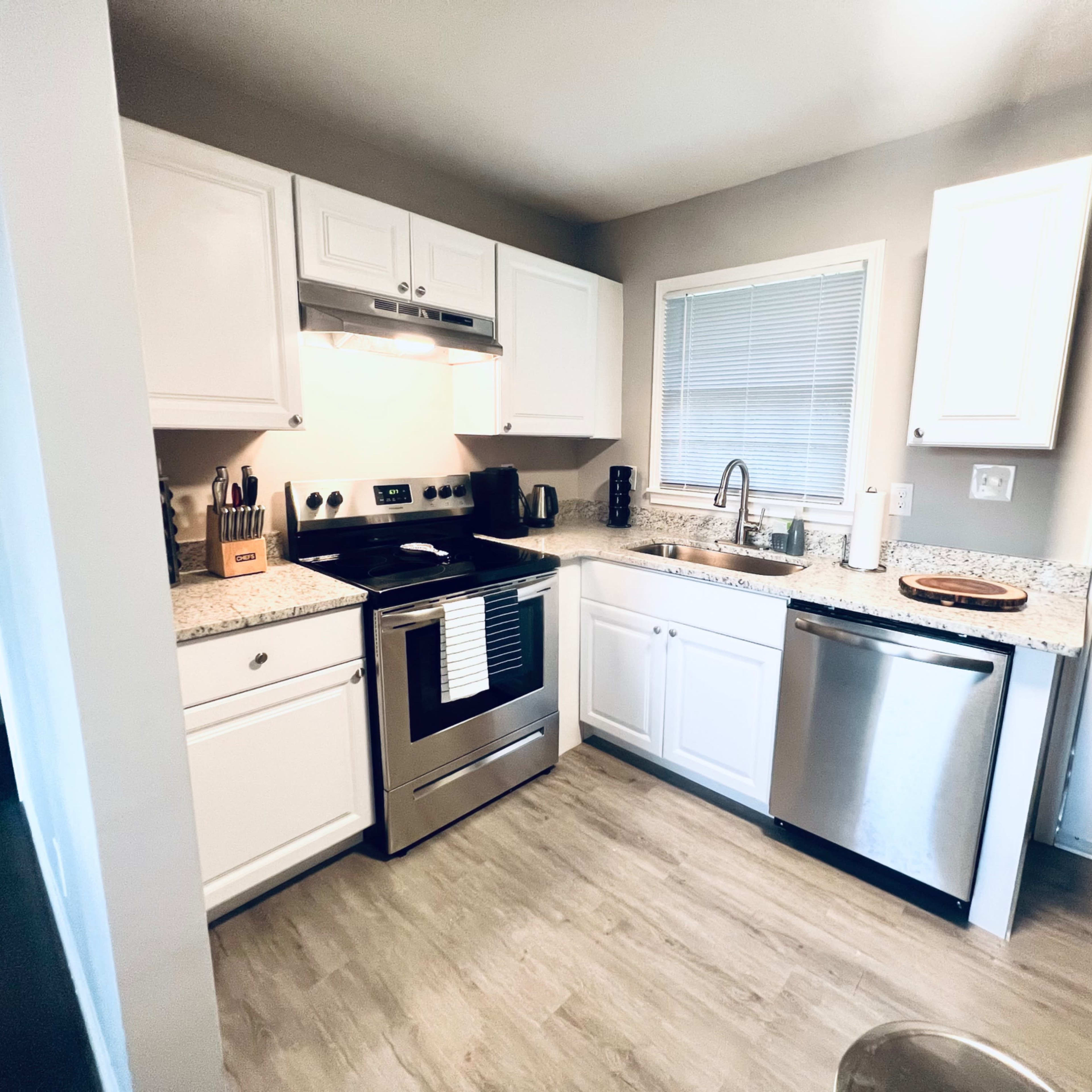 A compact kitchen features white cabinetry, a stainless steel refrigerator, and granite countertops.