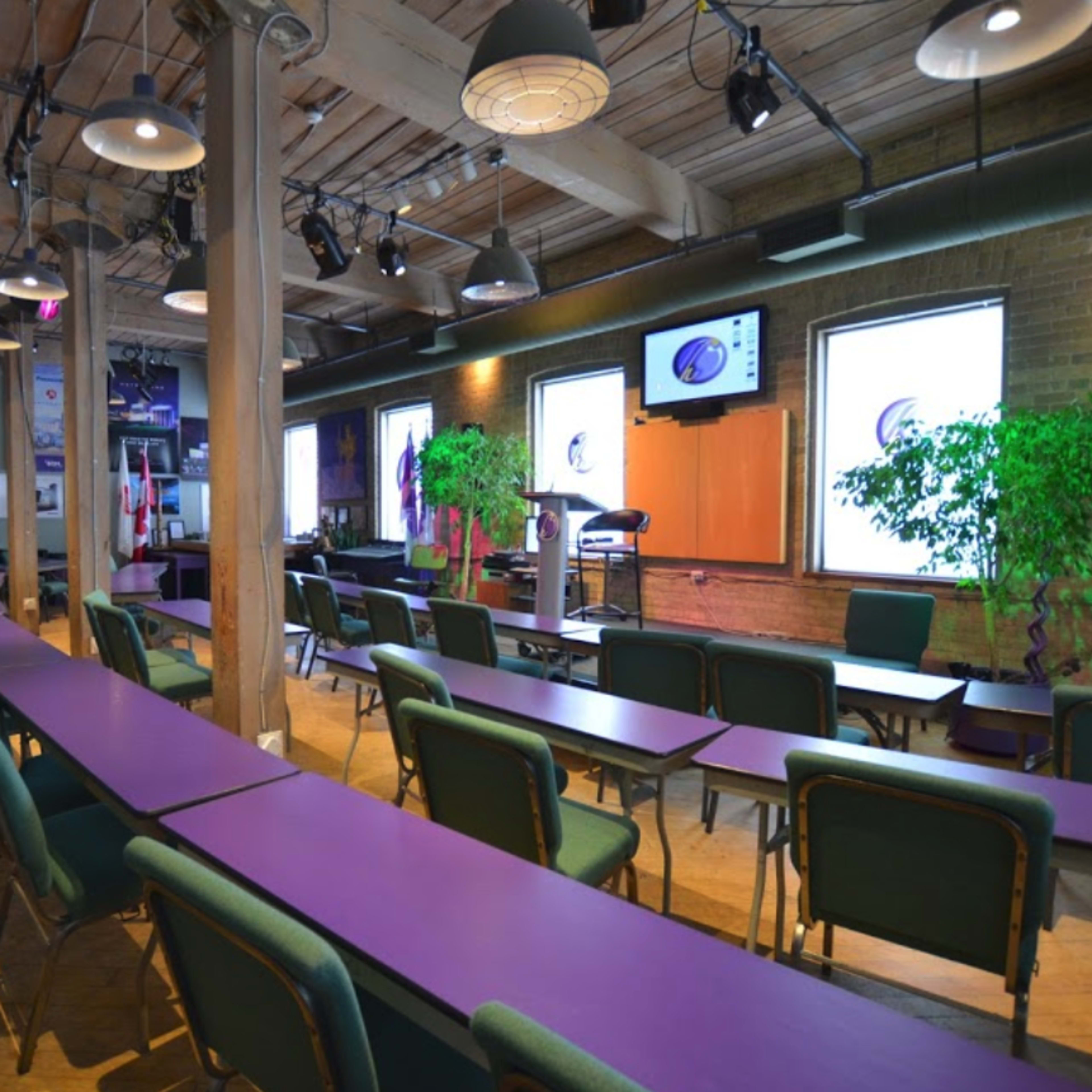 A classroom or meeting space with purple tables, green chairs, and large windows on one side.