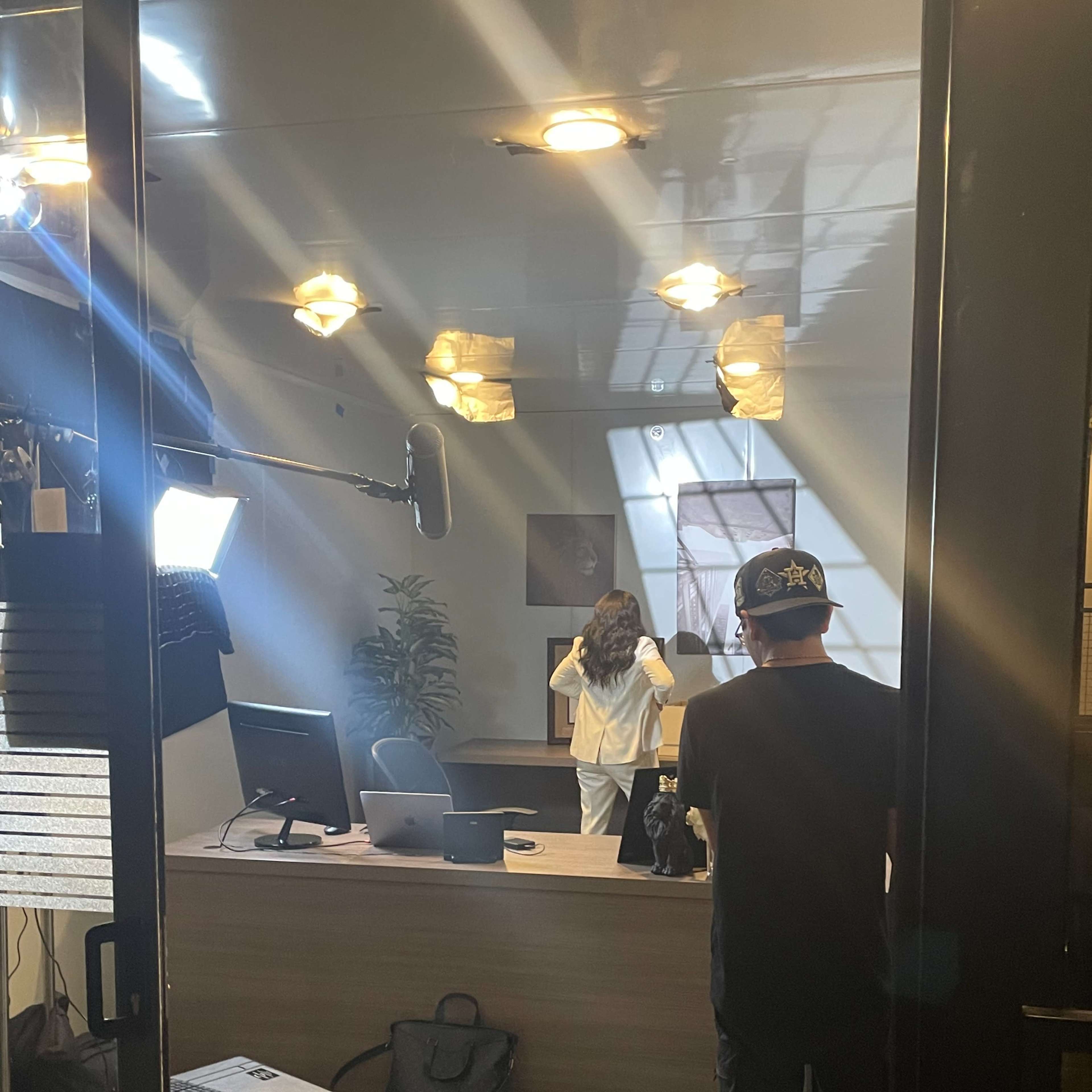 A person stands in an office setting while a camera operator captures the scene.