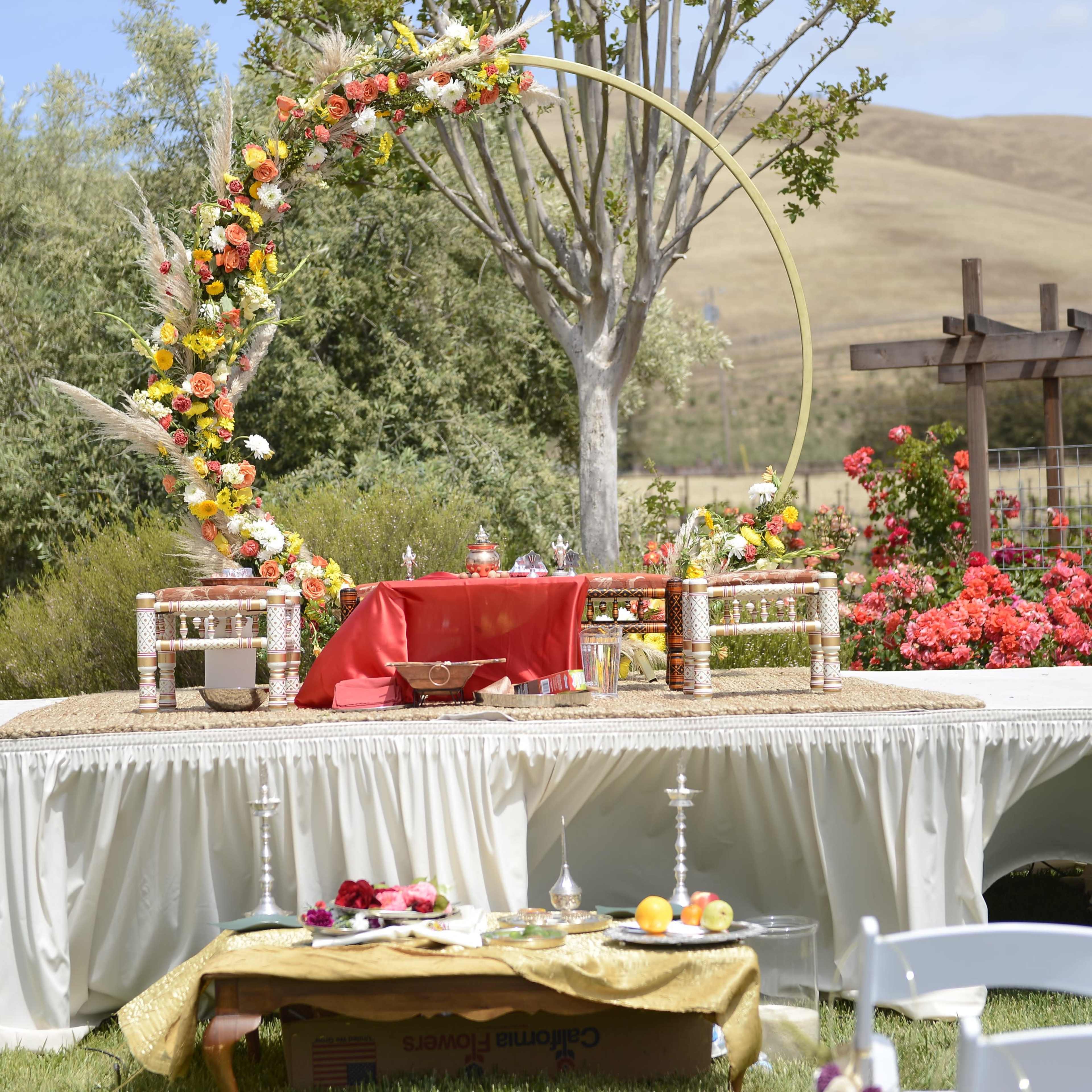 A decorated outdoor stage set with colorful floral arrangements, a red table, and surrounding greenery.