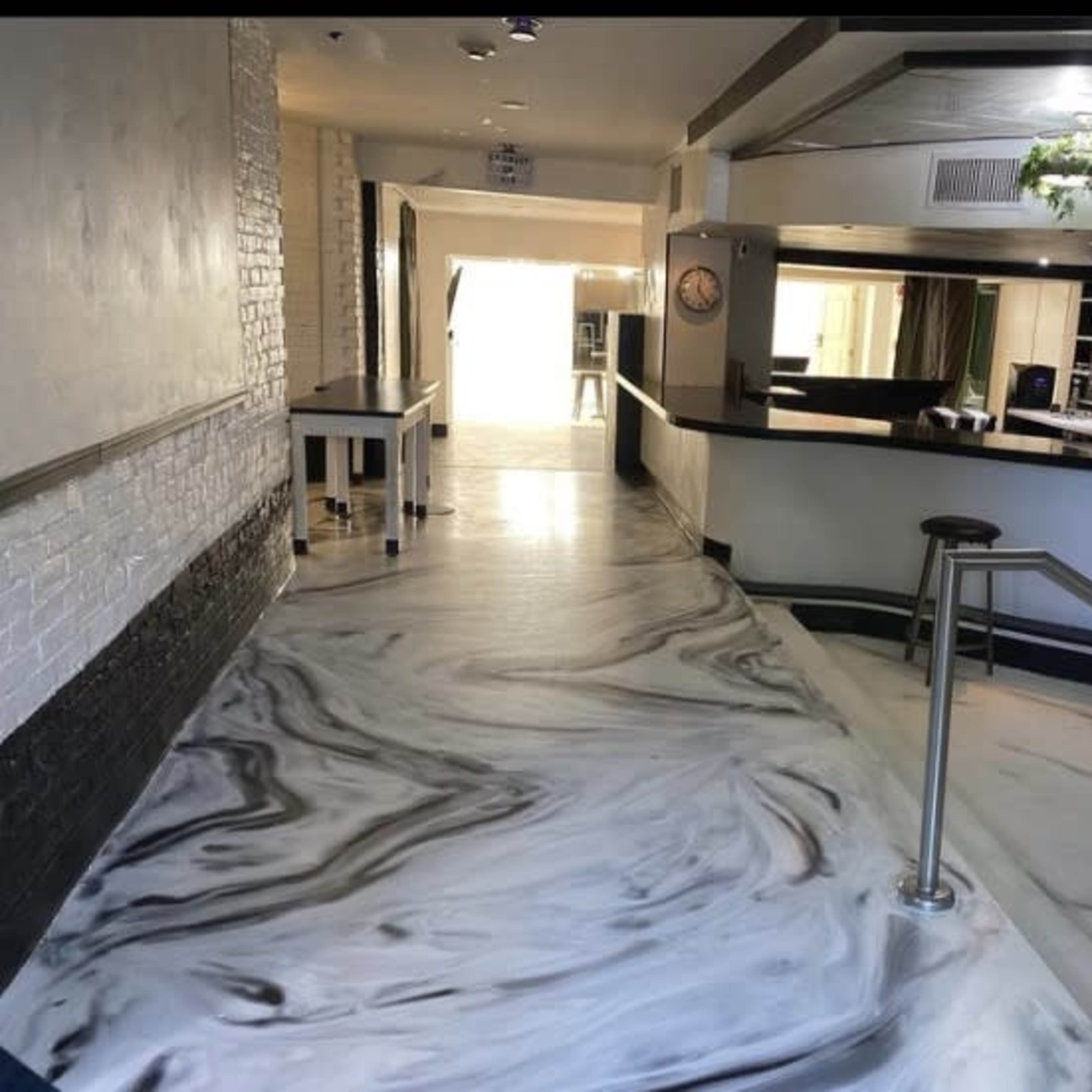 A hallway leading to a bar area with a marble-patterned floor and a row of stools along the counter.