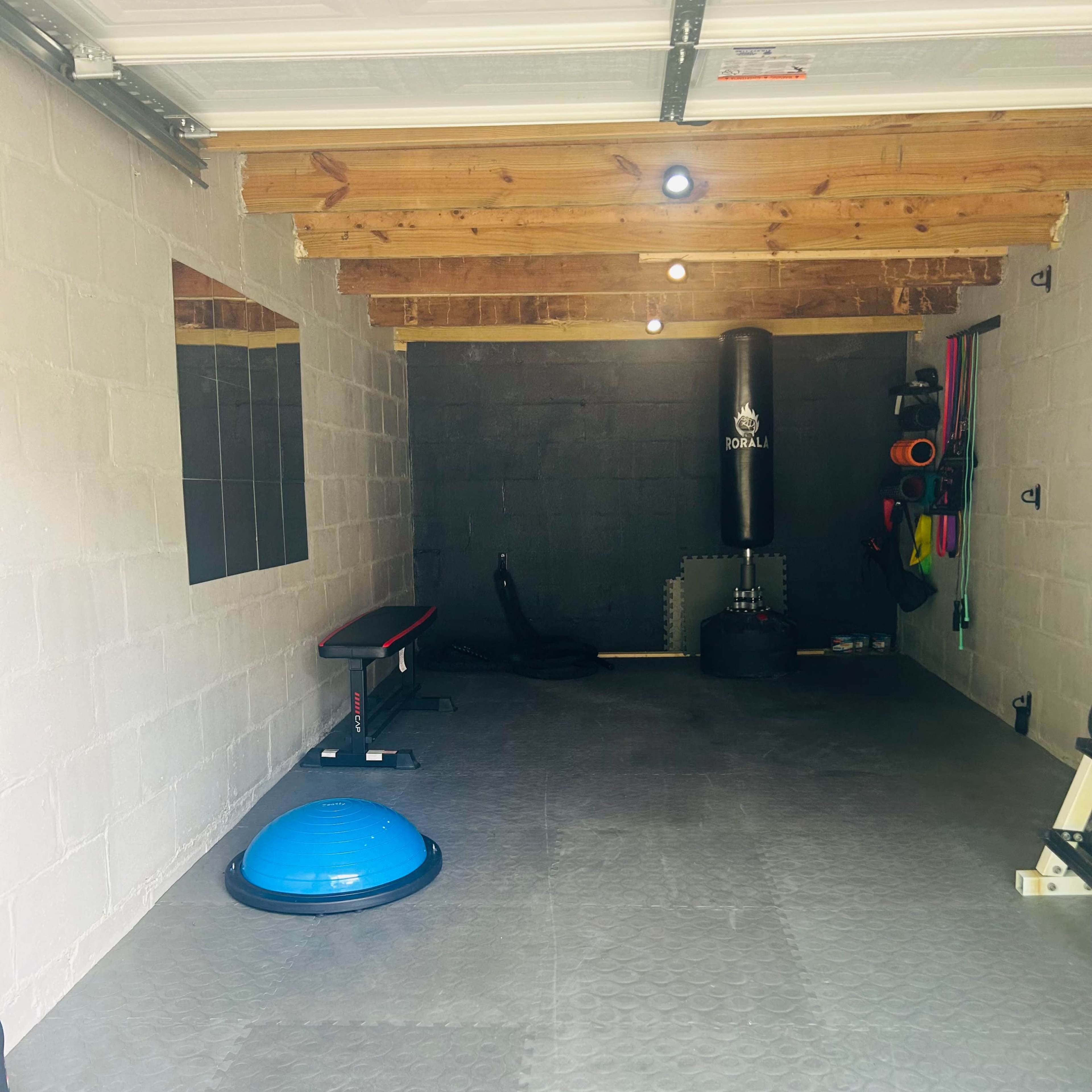 A spacious home gym features a punching bag, exercise equipment, and a balance trainer on a rubber floor under exposed wooden beams.