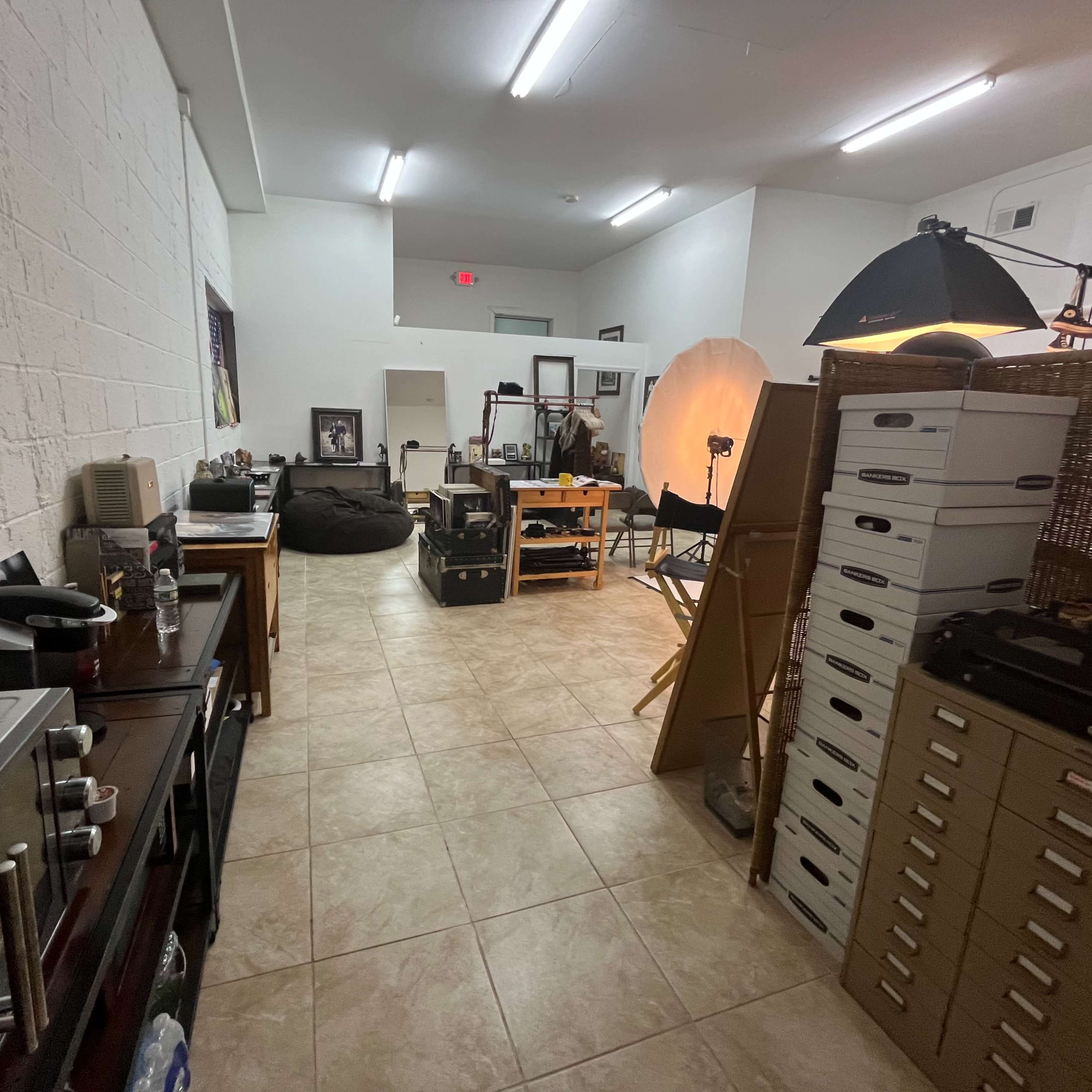 A spacious room with tiled floors, featuring various furniture items, photography equipment, and storage boxes.