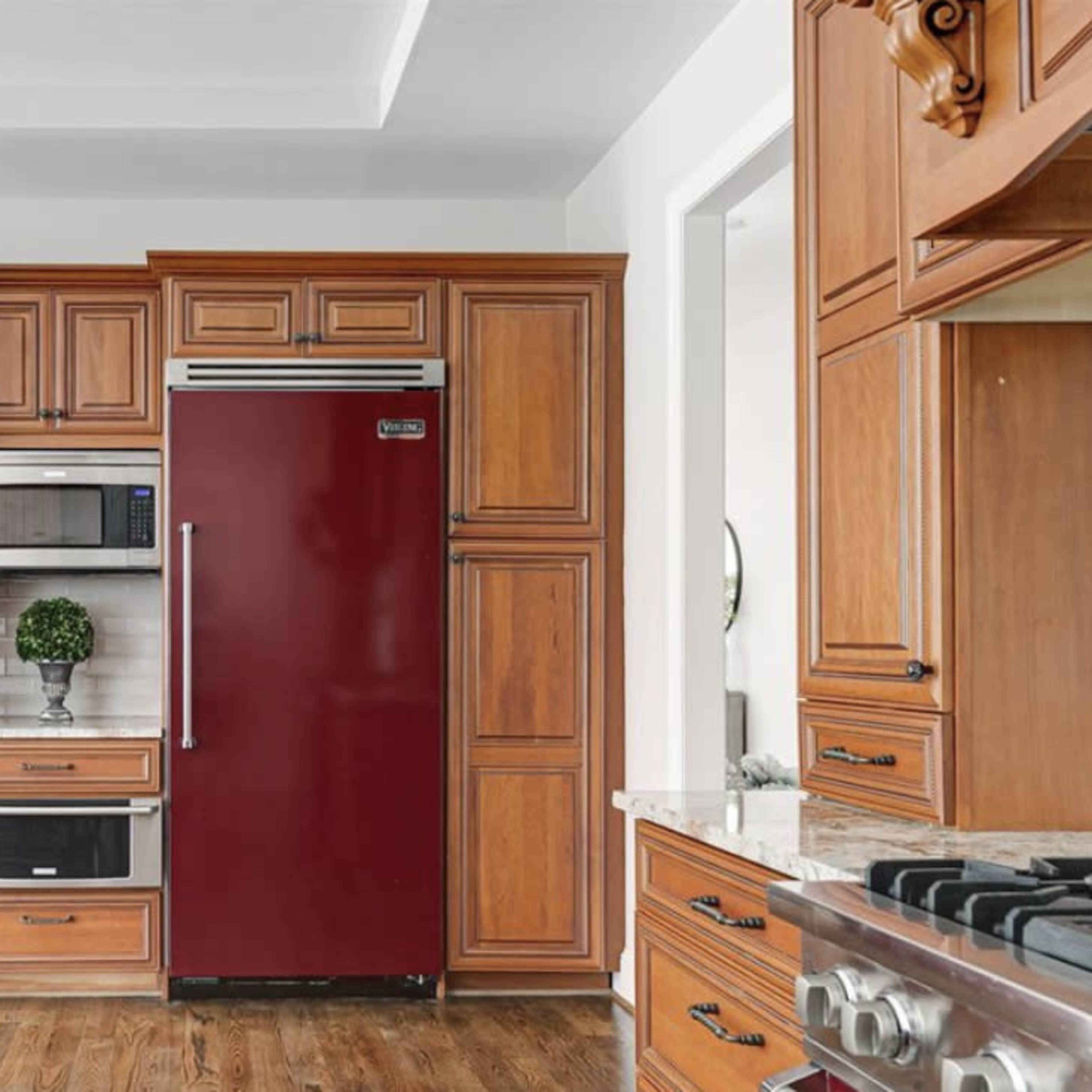 A kitchen with two red refrigerators flanking a built-in microwave and a small plant on a countertop beneath wooden cabinetry.