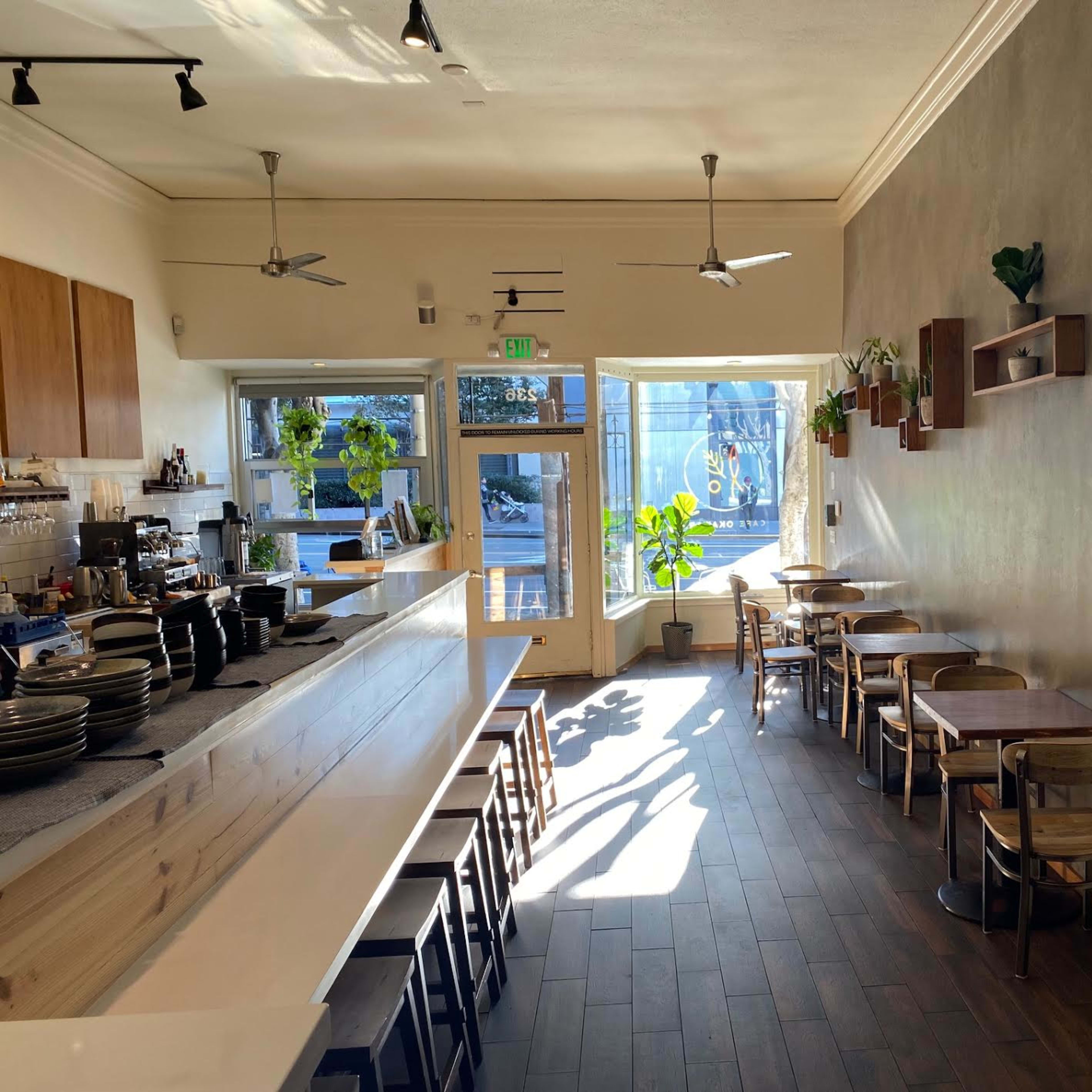 A modern café with a long wooden counter, several tables, and large windows letting in natural light.