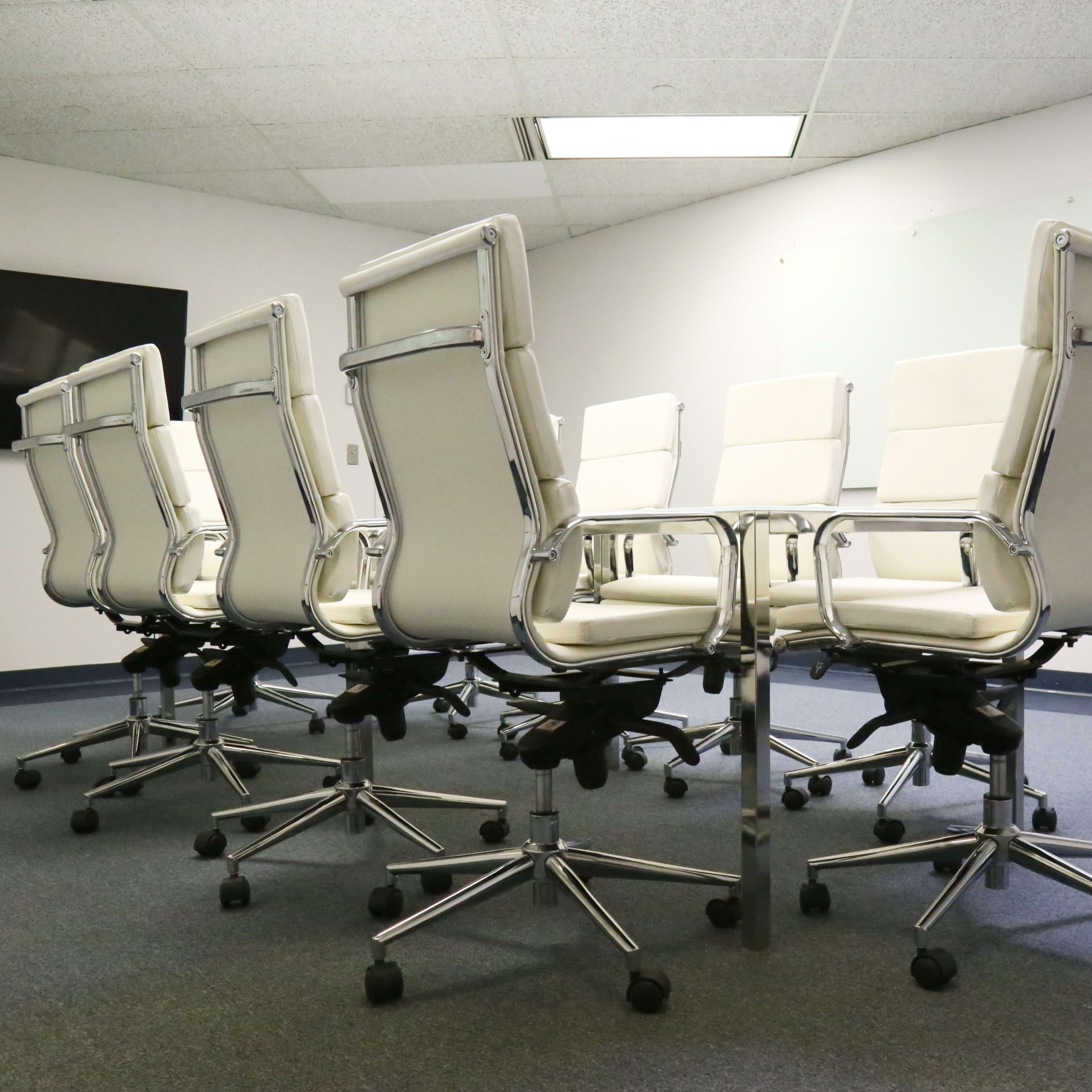 A row of white leather office chairs on rolling bases is arranged around a conference table in a meeting room.