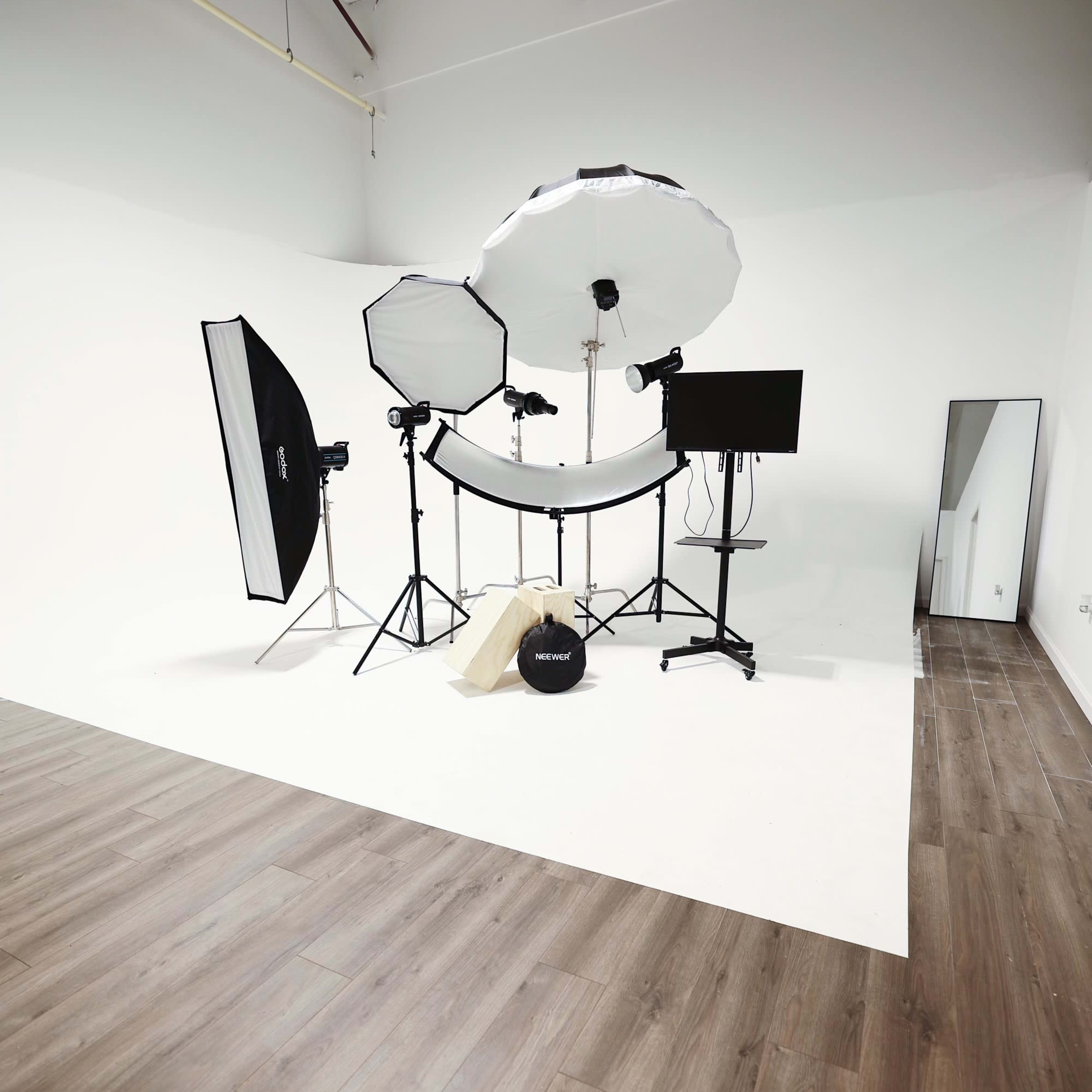 A photography studio is set up with various lighting equipment, backdrops, and a mirror against a plain white wall.