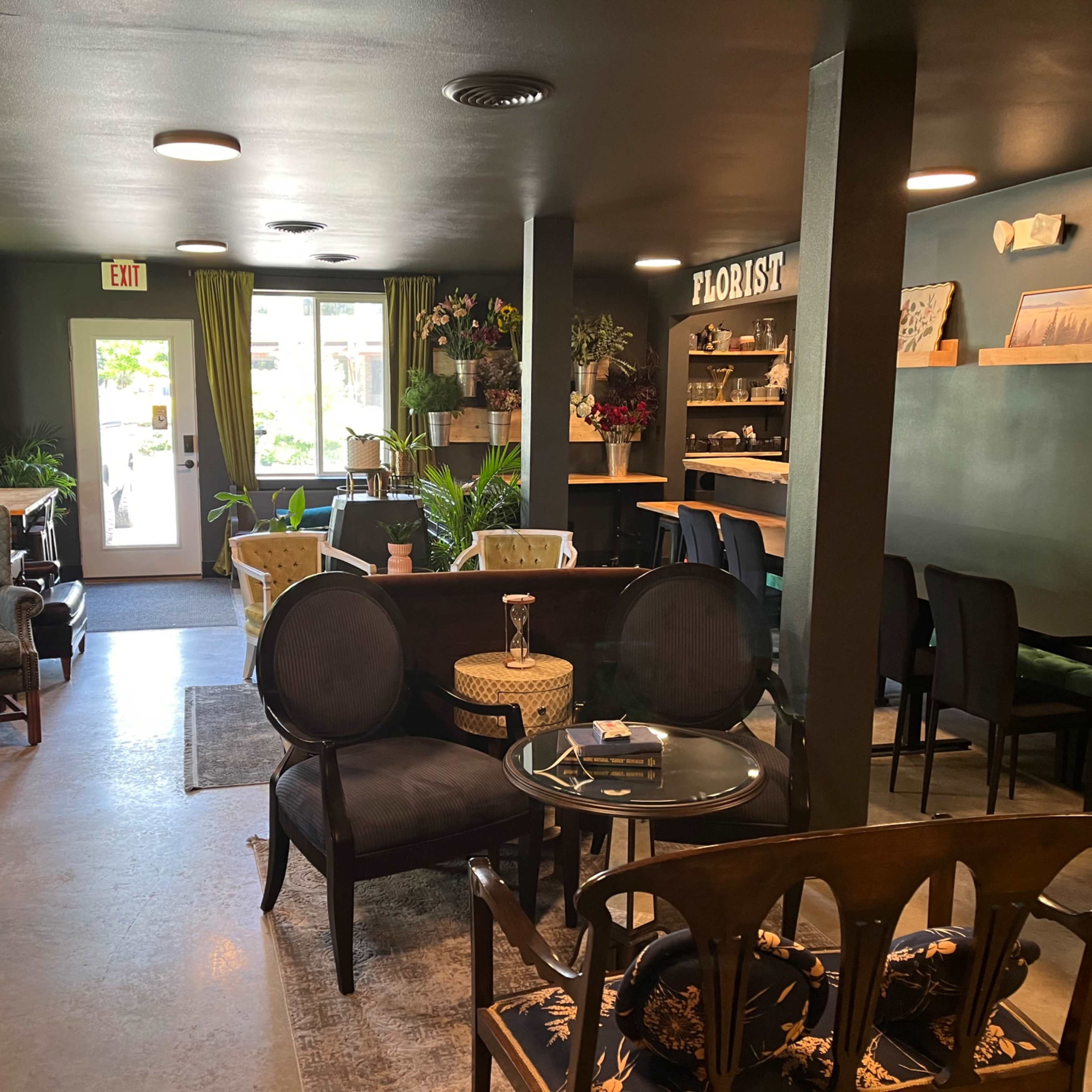 A cozy floral shop interior with various seating arrangements and decorative plants, complemented by a small counter area.
