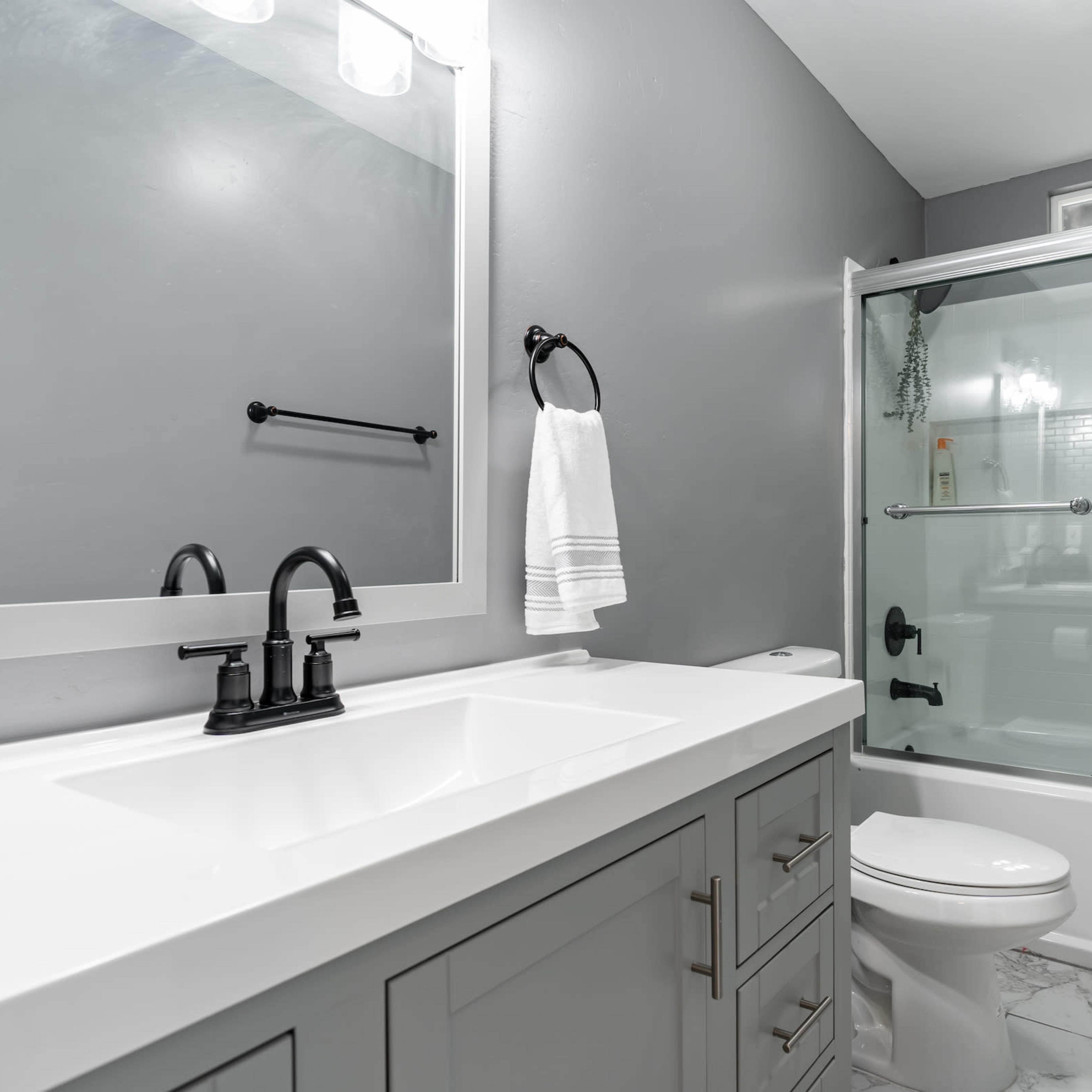 A modern bathroom featuring a gray color scheme, a double-sink vanity with a white countertop, and a glass-enclosed shower.
