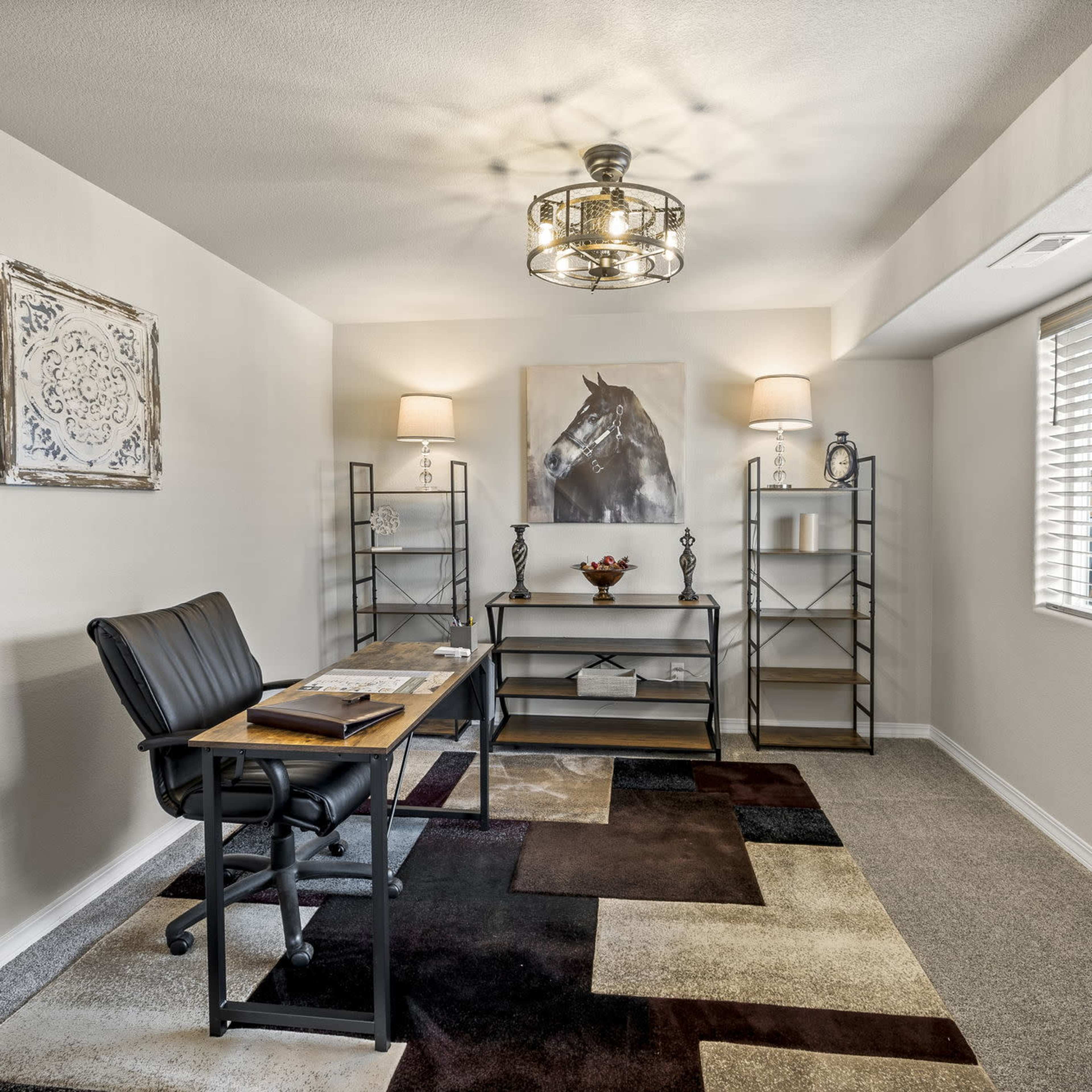 A well-lit home office featuring a black desk with a chair, bookshelves, and artwork of a horse on the wall.