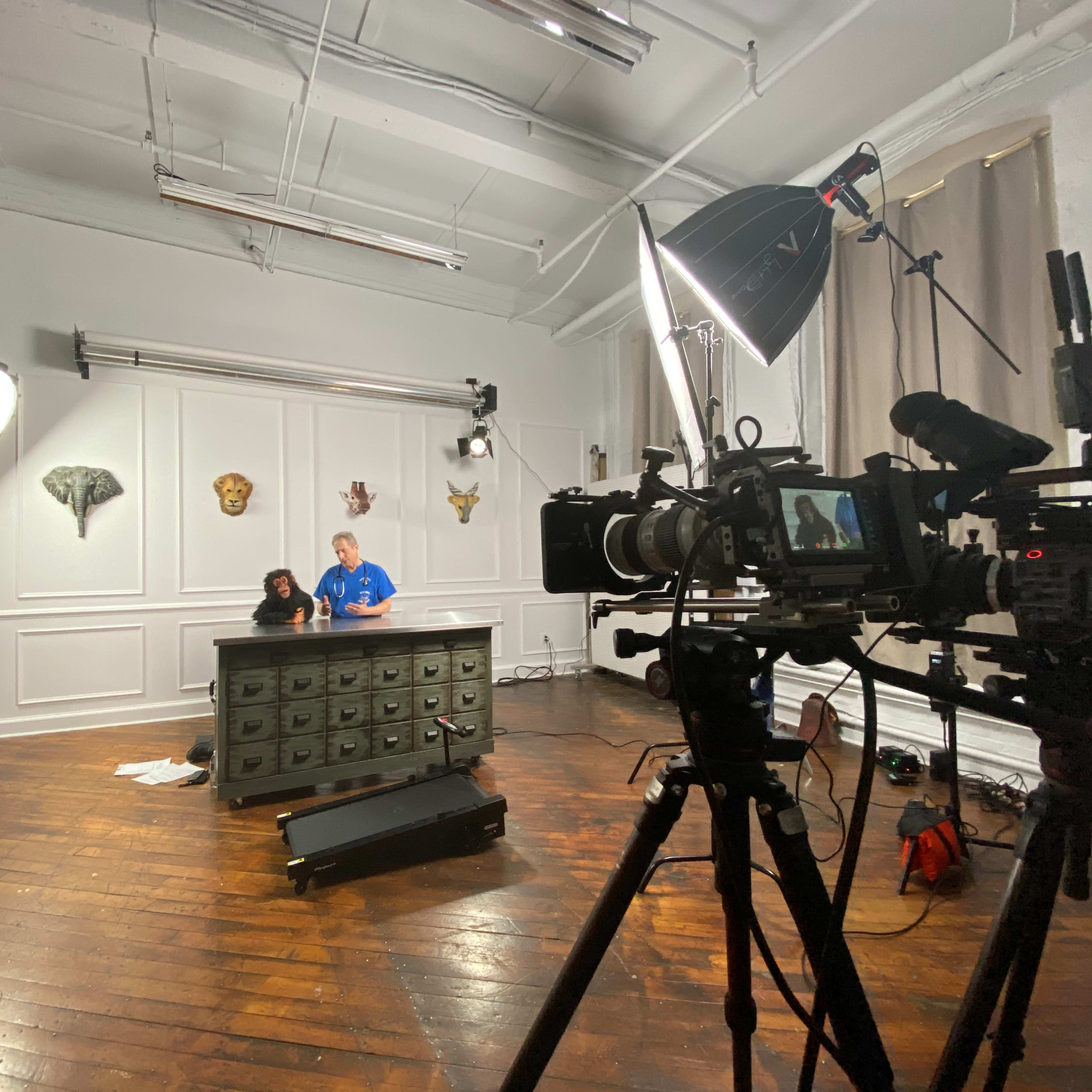 A film crew sets up equipment in a studio featuring a large wooden desk and various lighting setups.