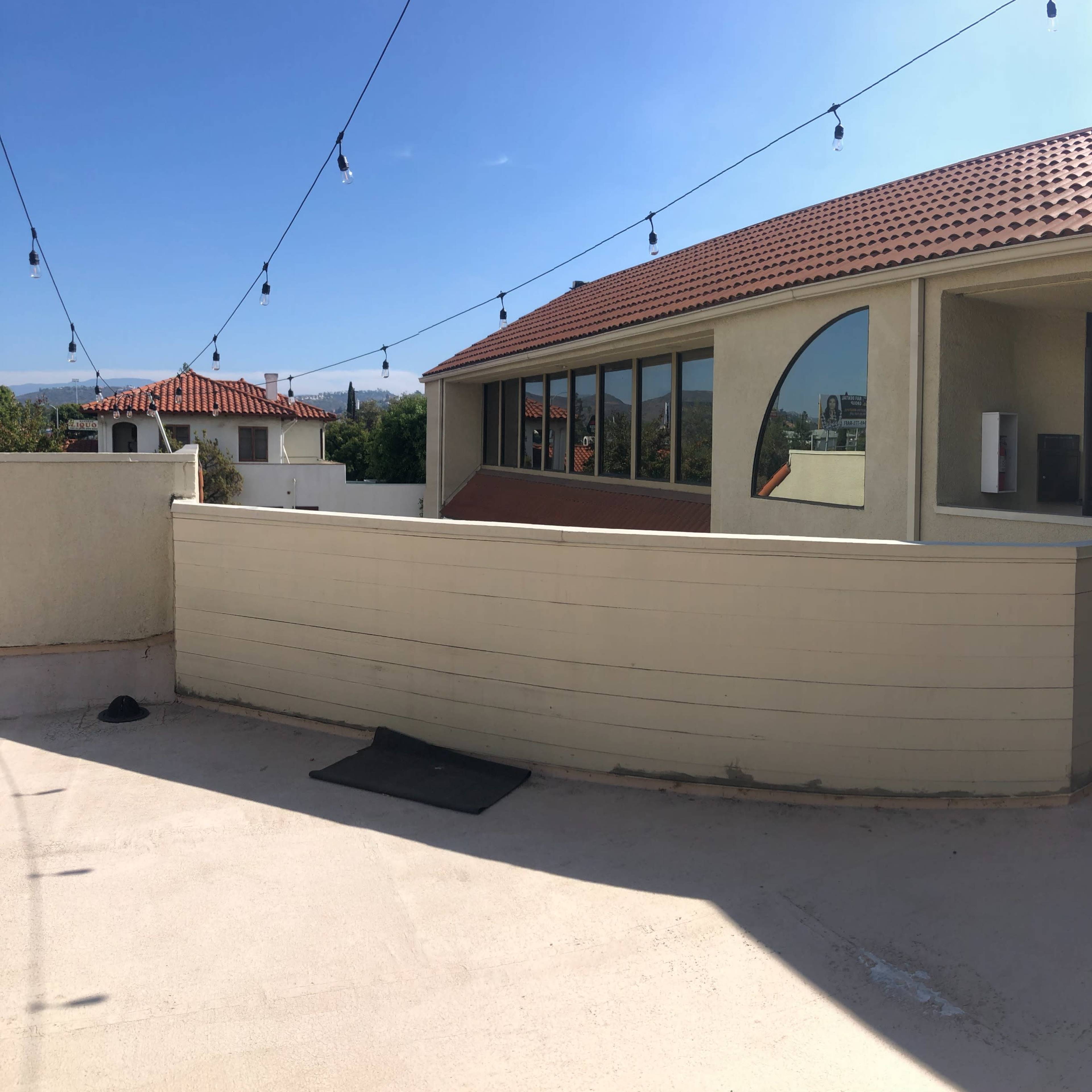 A panoramic view of a building with a curved window and string lights overhead, situated on a rooftop terrace.