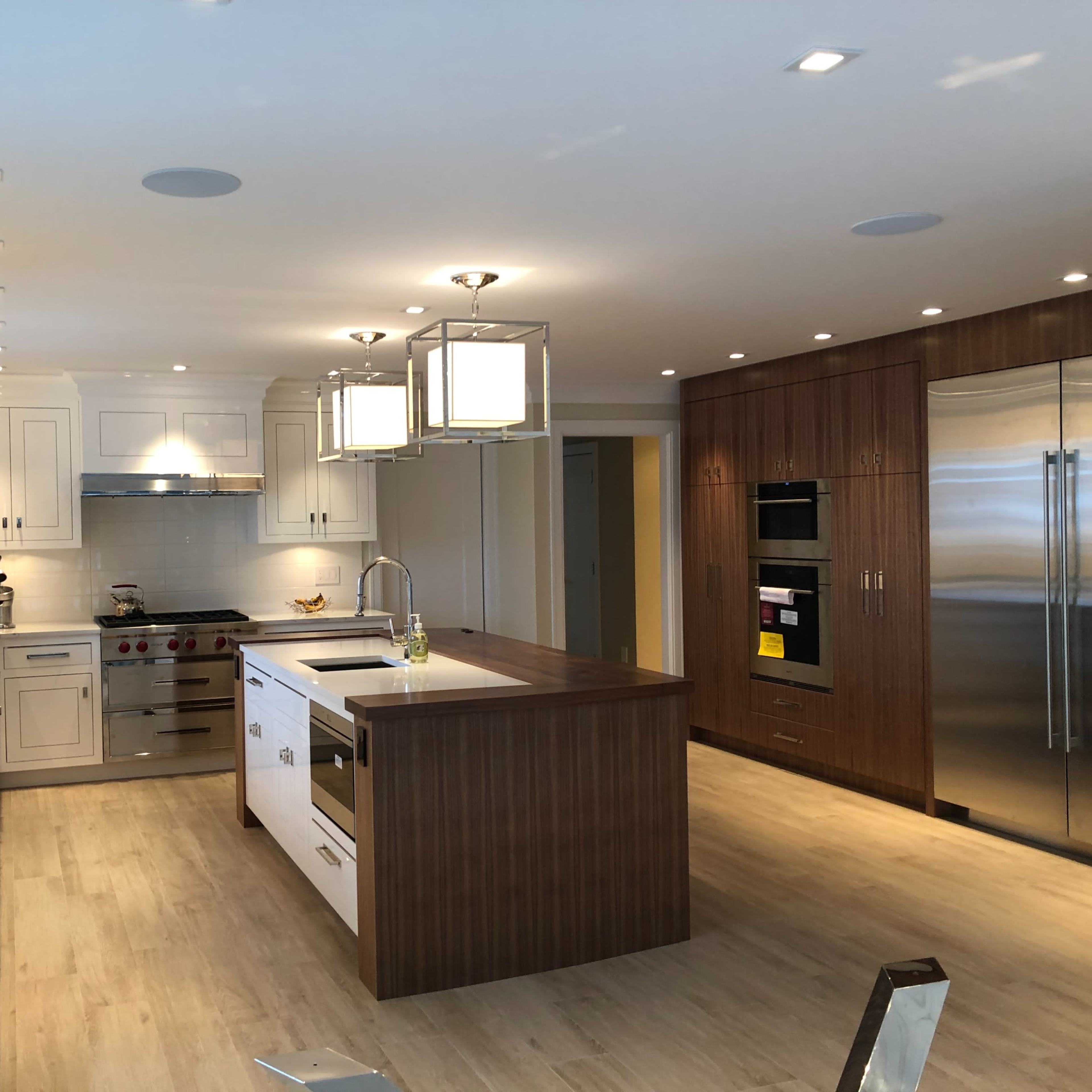 A modern kitchen with white cabinets, a large island, stainless steel appliances, and two hanging light fixtures.