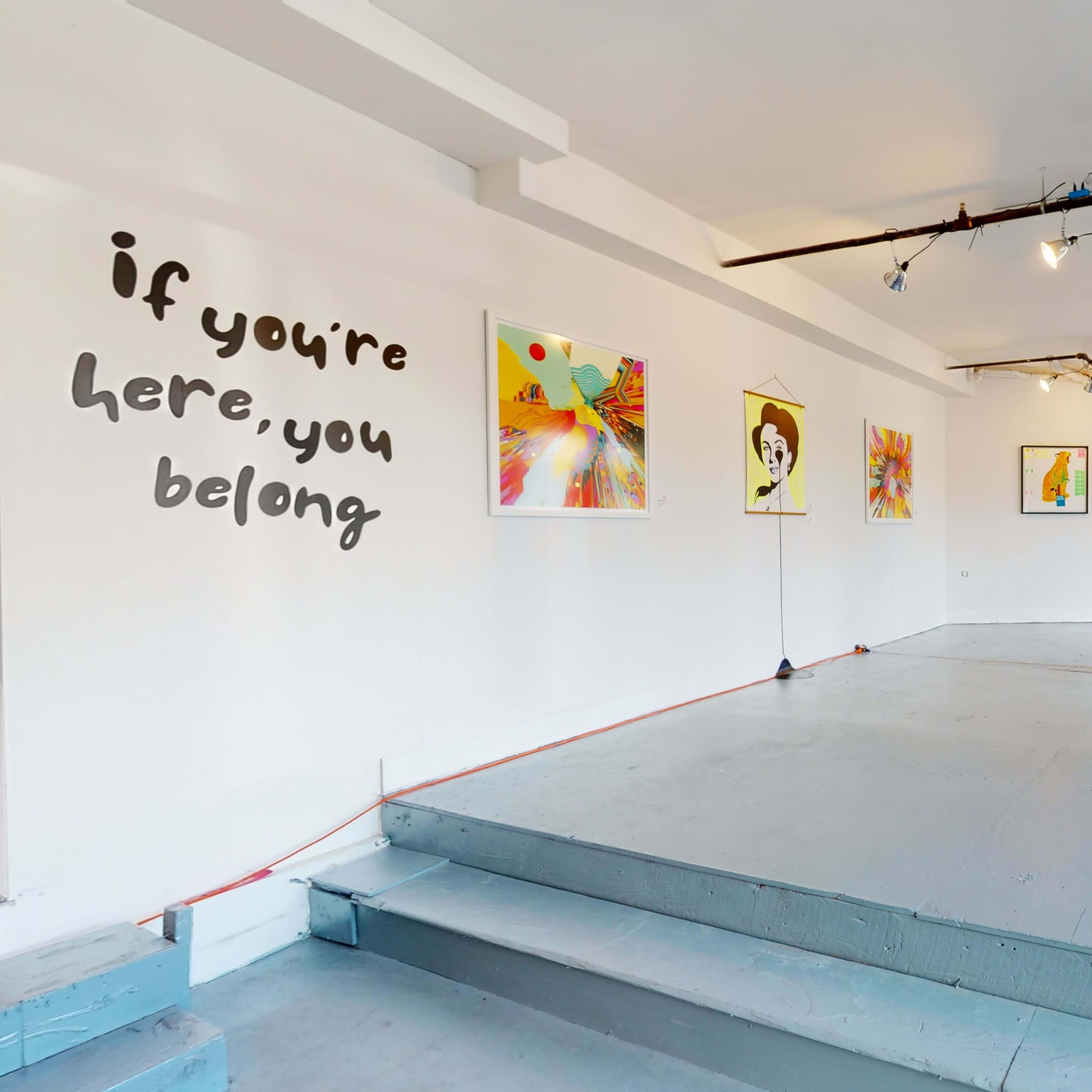 A spacious art gallery with colorful paintings displayed on the white walls and a minimalist pedestal in the center.