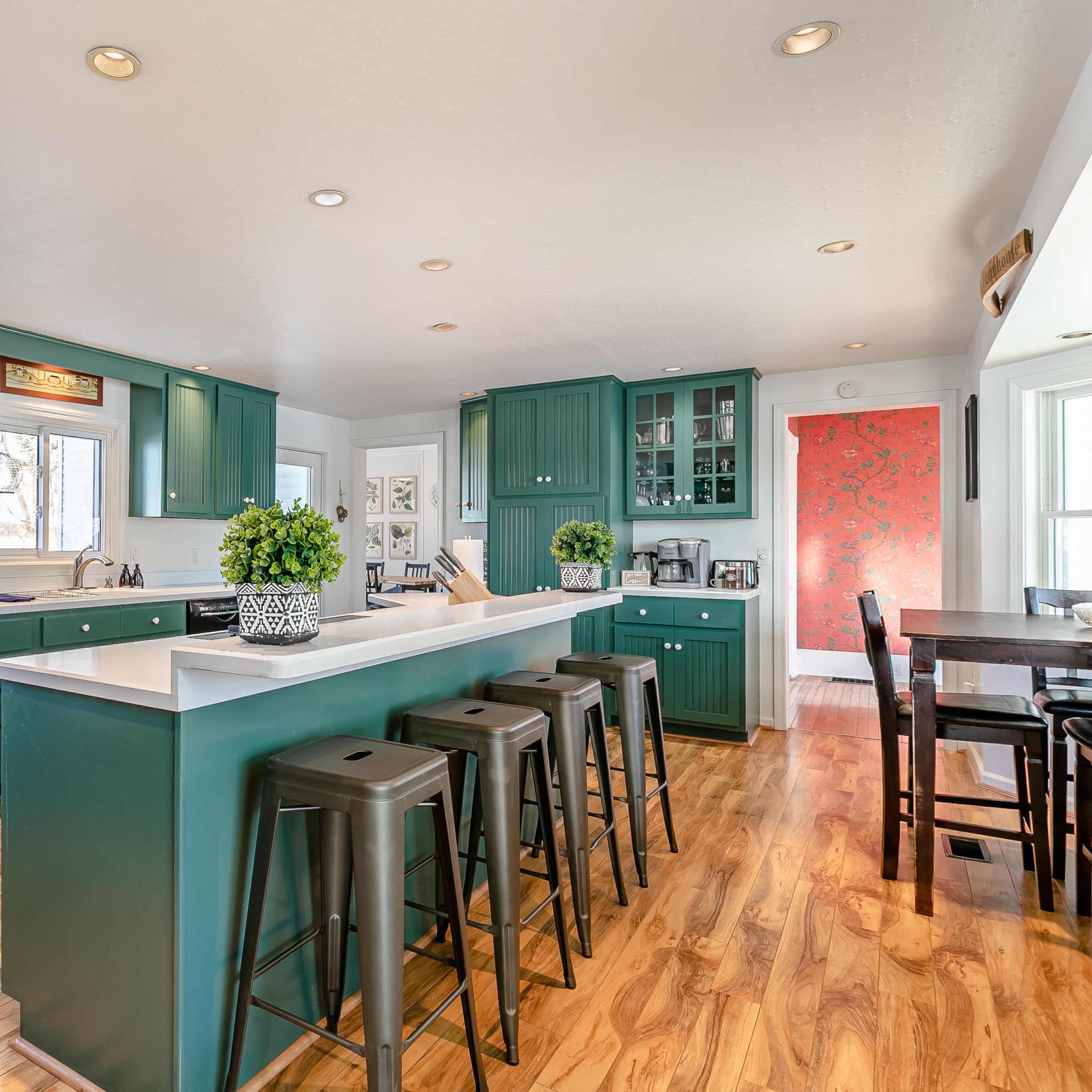 A modern kitchen with green cabinets, a central island with bar seating, and light-colored countertops.