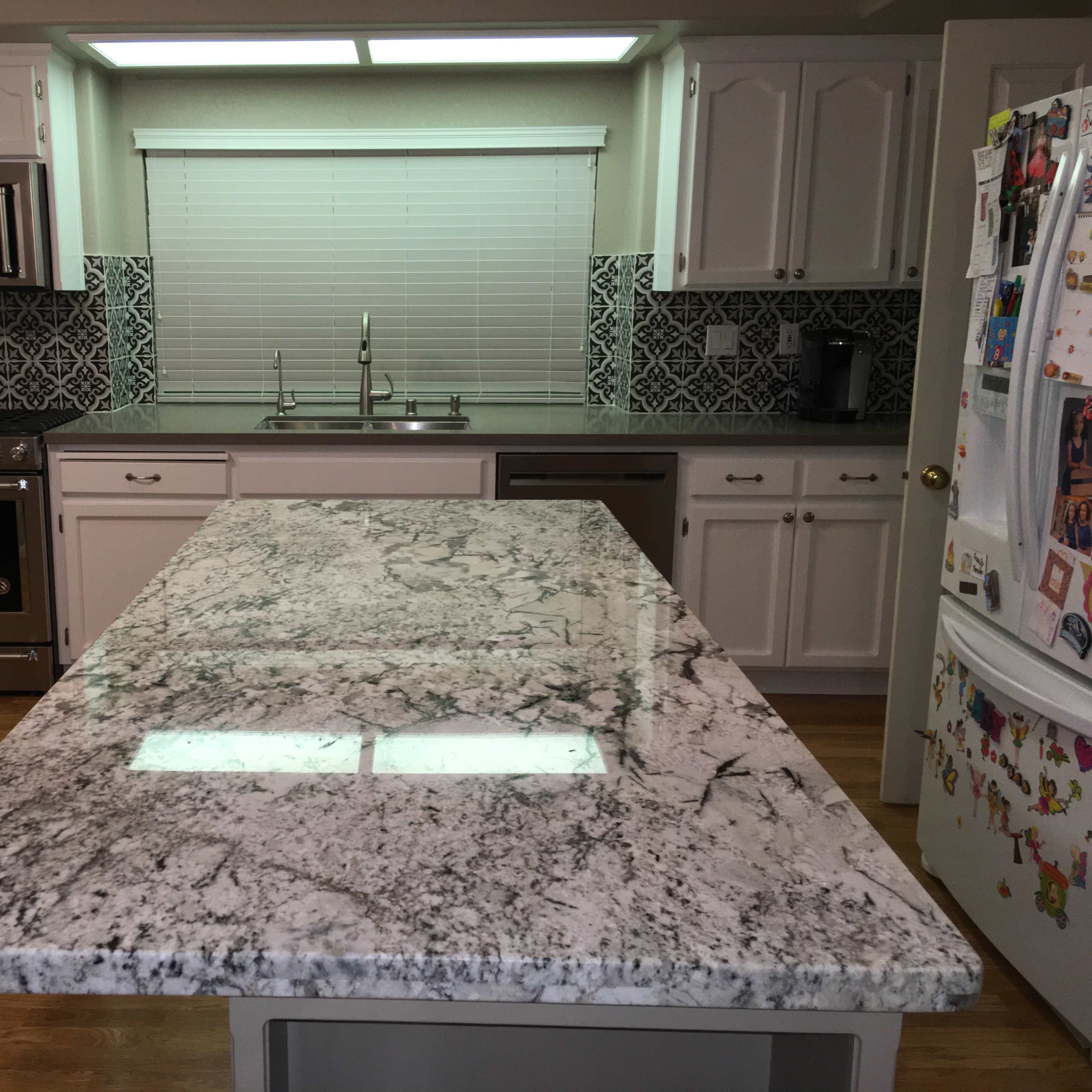 A modern kitchen with a granite countertop island, stainless steel appliances, and patterned backsplash tiles.