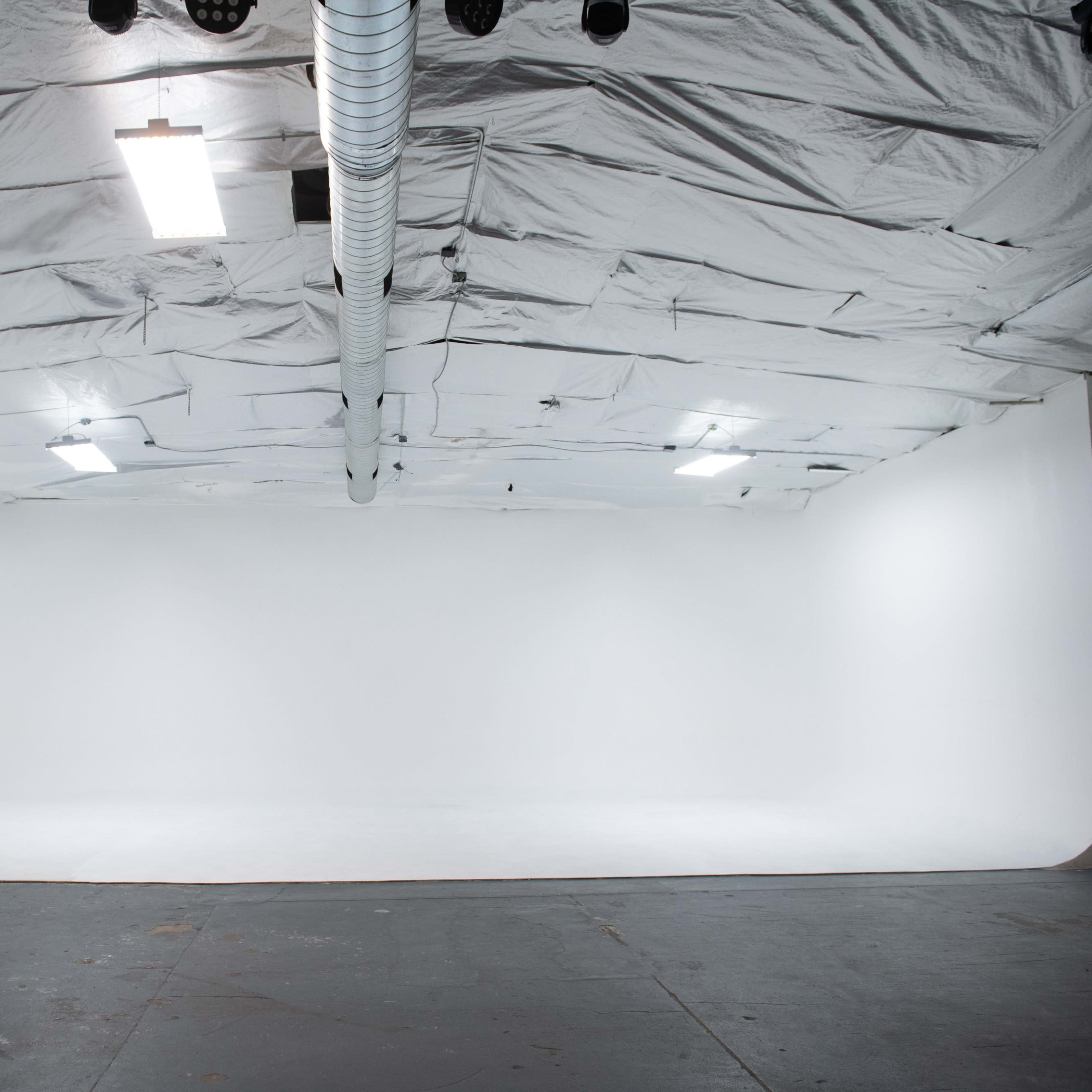 An empty studio space with a white curved backdrop, illuminated by overhead lights.