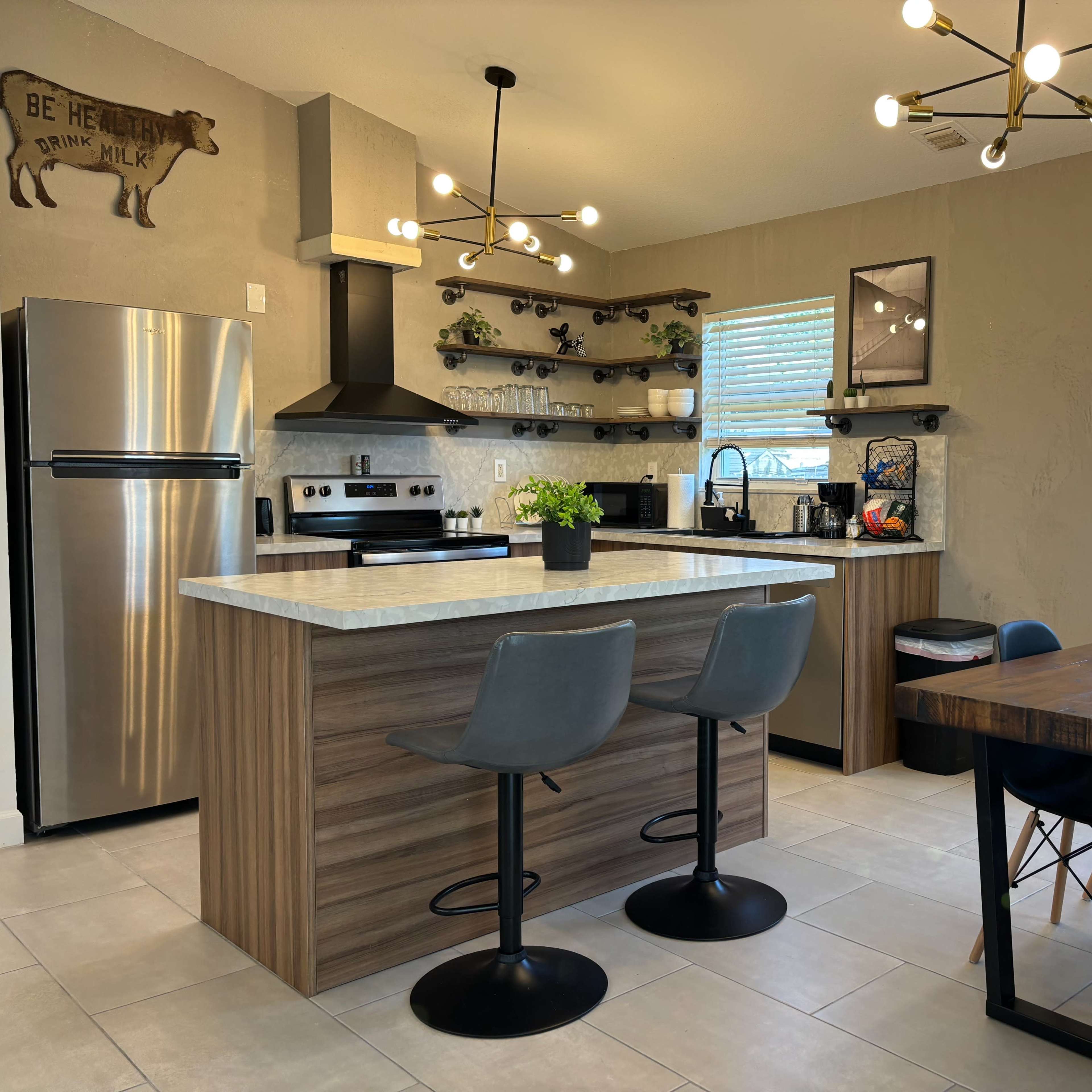 A modern kitchen with a central island, stainless steel appliances, open shelving, and a dining table nearby.