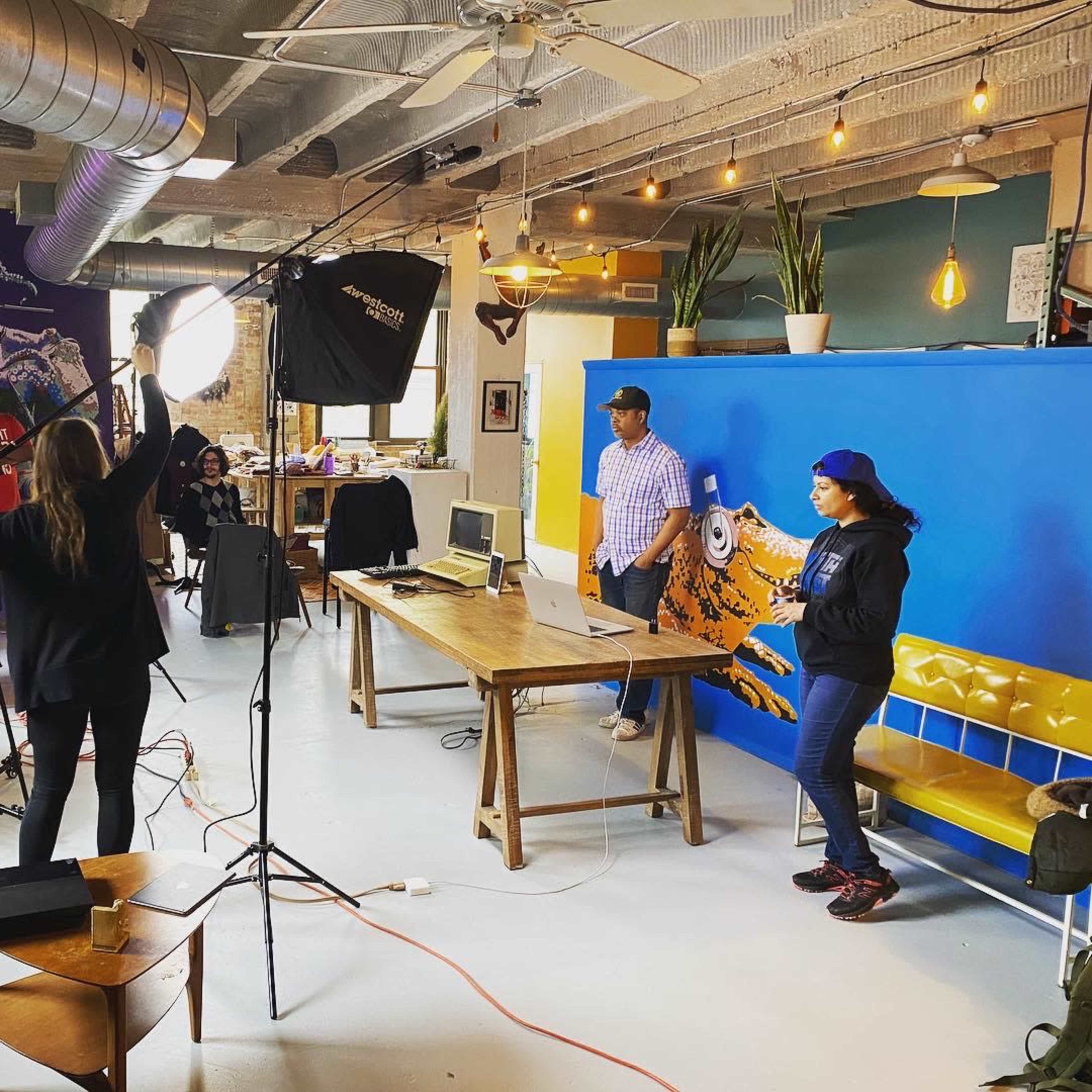 A group of people is setting up equipment for a photo or video shoot in a brightly colored creative workspace.