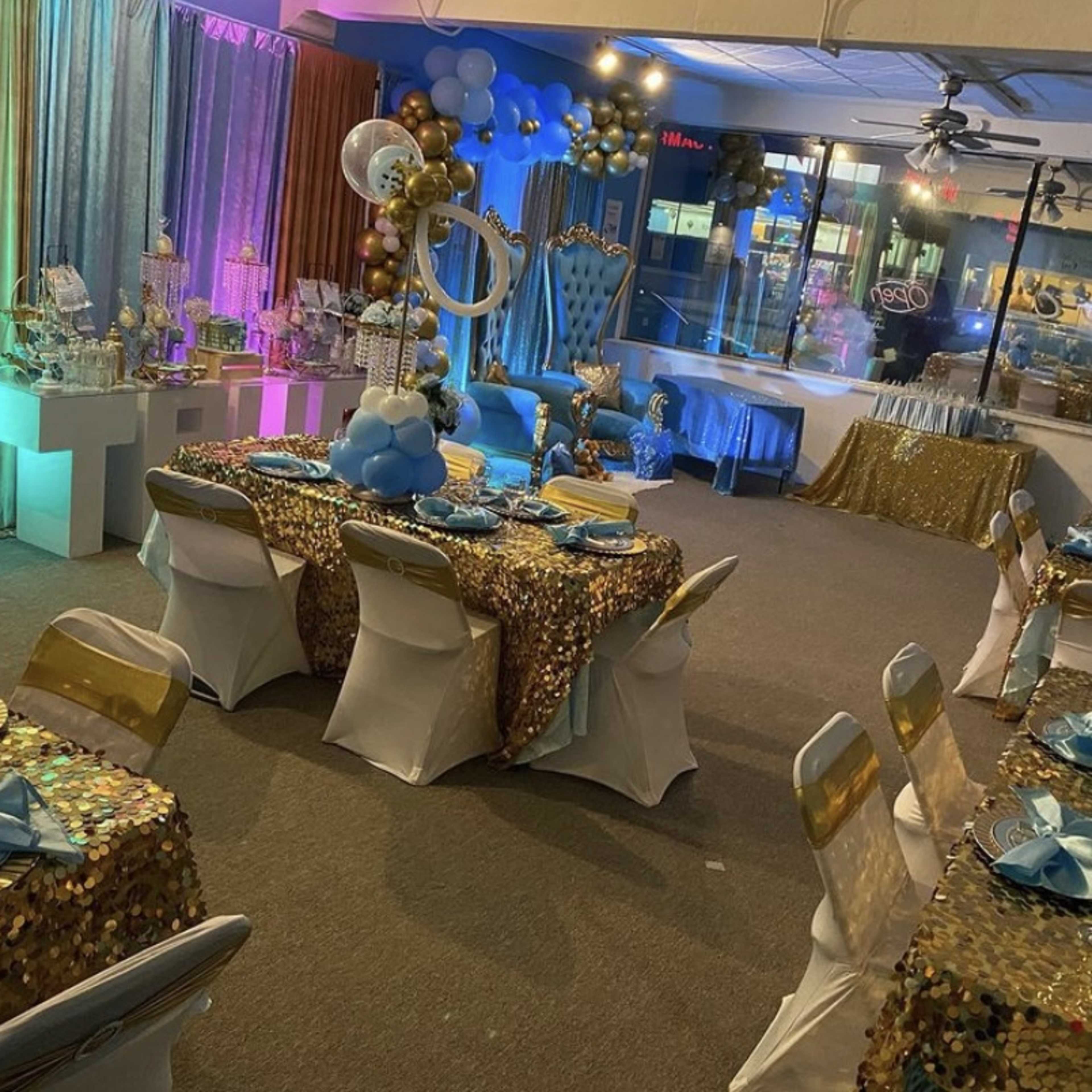 A banquet hall decorated for an event, featuring tables with sequined tablecloths, balloons, and various decorative arrangements.