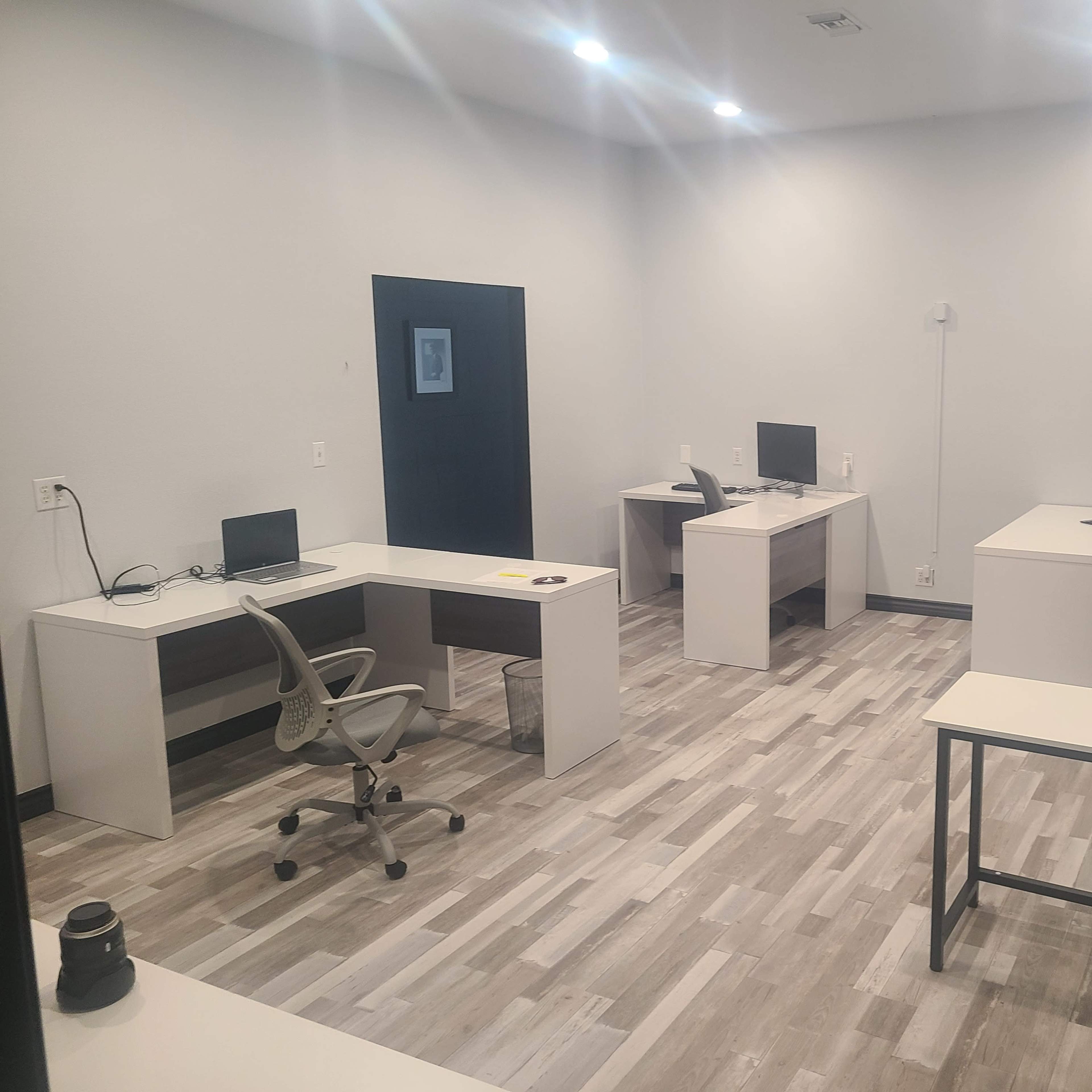 A modern office space with several workstations, each equipped with a computer and office chair, arranged in a well-lit, minimalist environment.